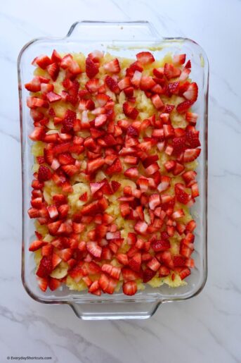 chopped strawberries on top of crushed pineapple in baking dish