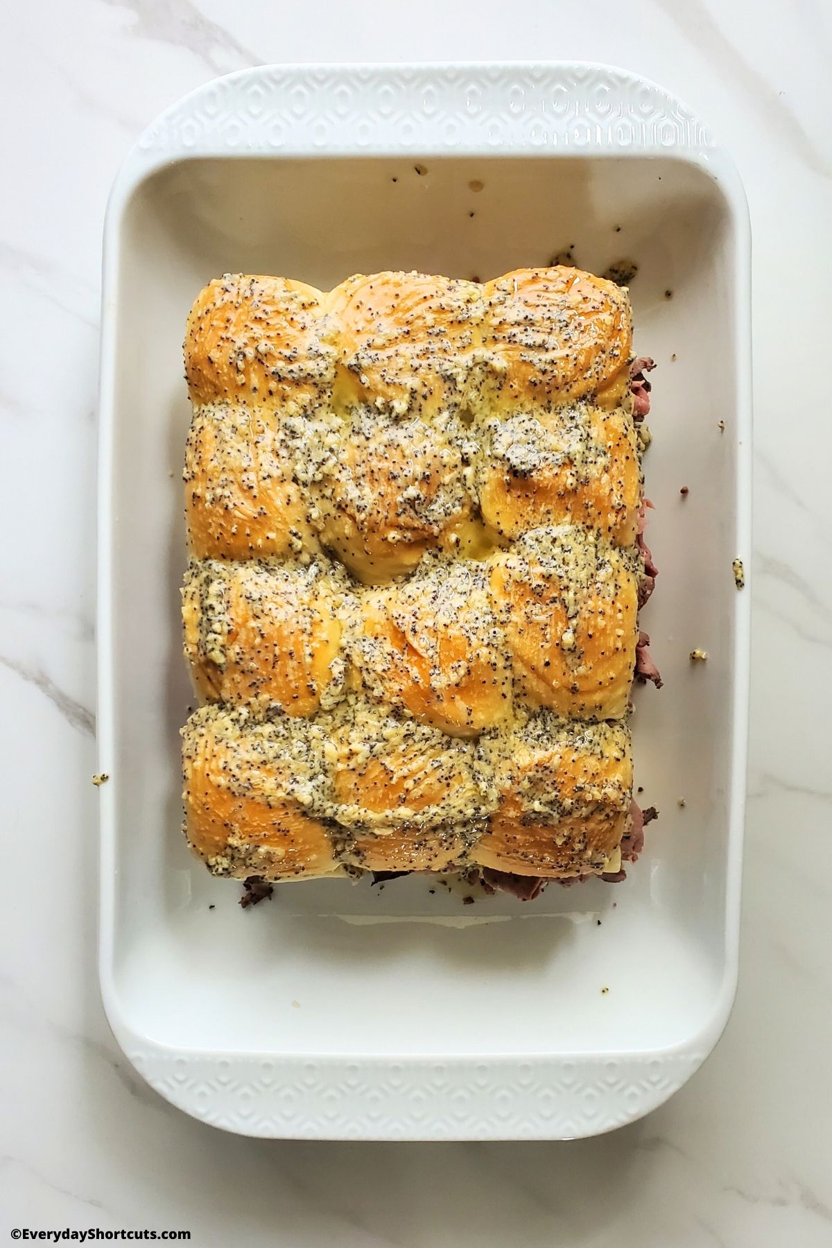 dijon mustard with poppy seeds brushed on top of hawaiian rolls in a baking dish