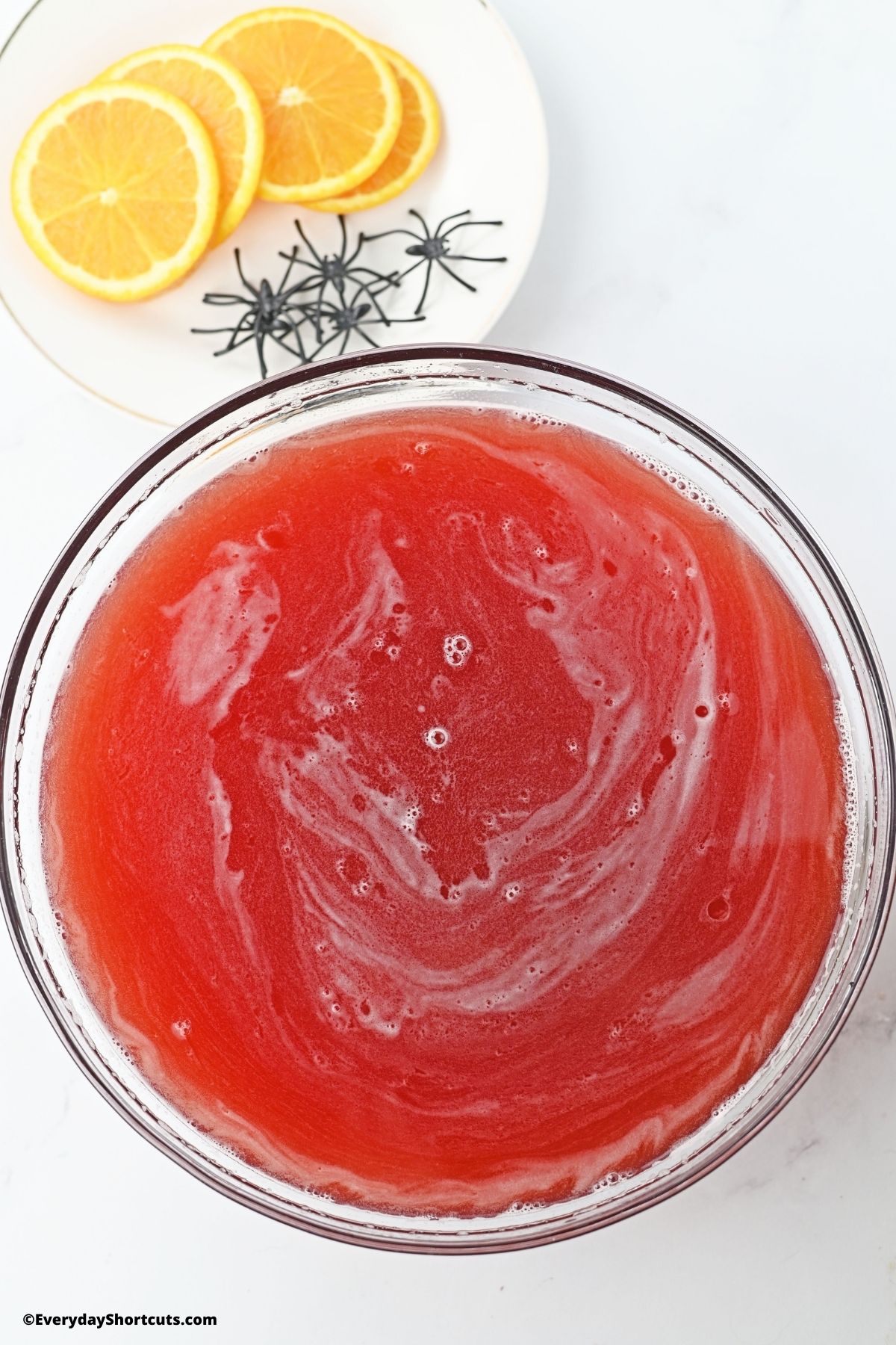 red alcoholic drink in a serving bowl with orange slices and plastic spiders on the side