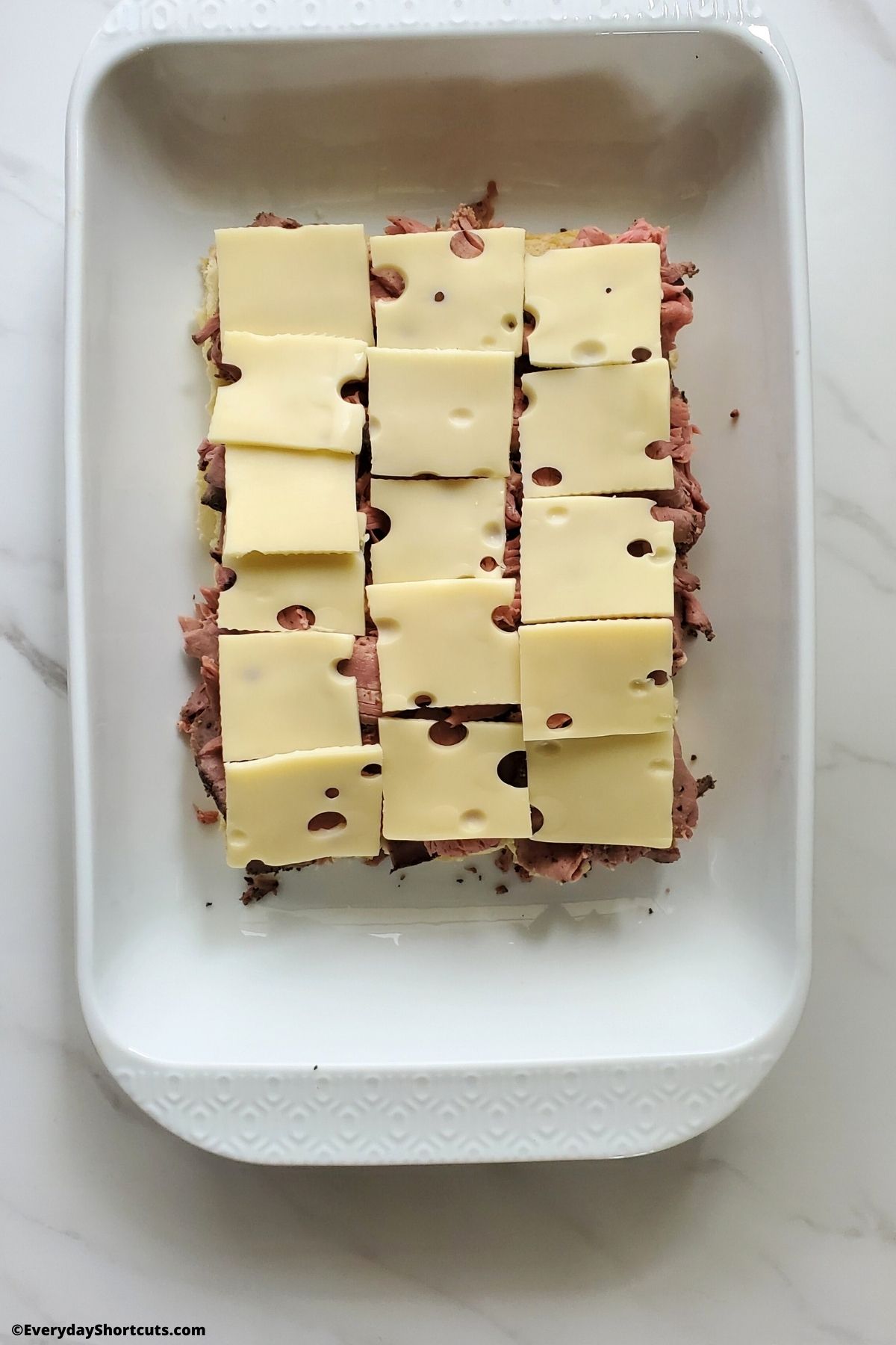 swiss cheese on top of roast beef in a pan