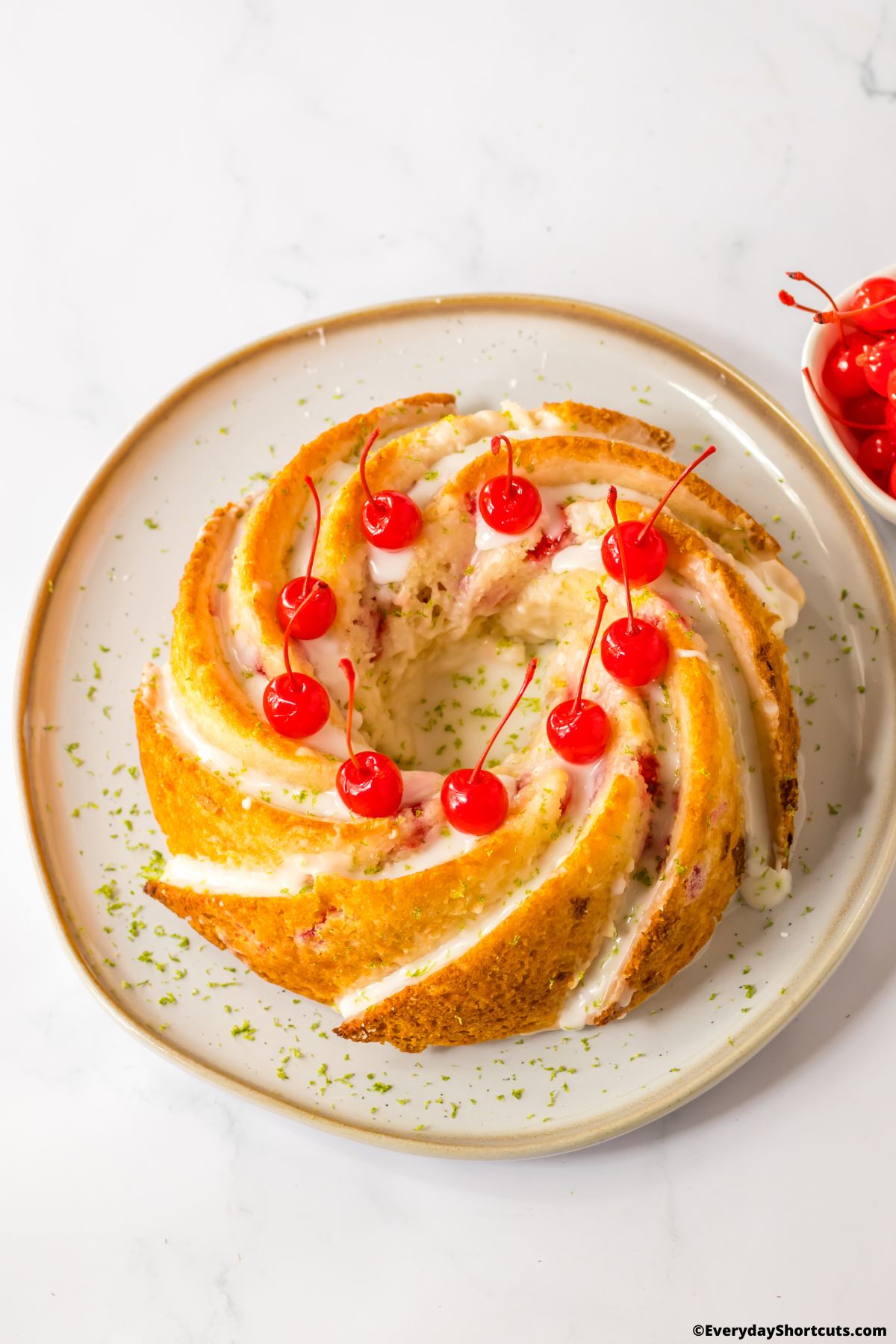 whole shirley temple bundt cake on a plate garnished with cherries and lemon zest