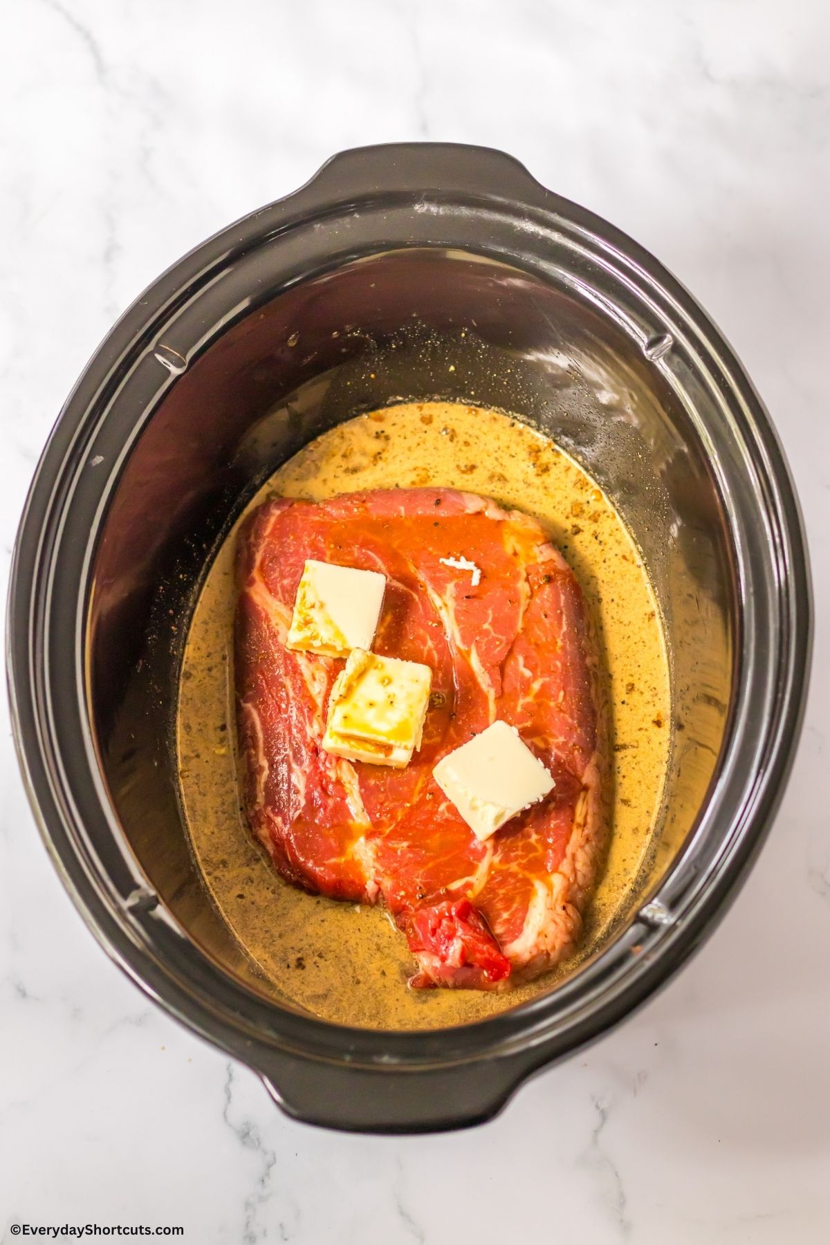 chuck roast in slow cooker with gravy mix and butter on top