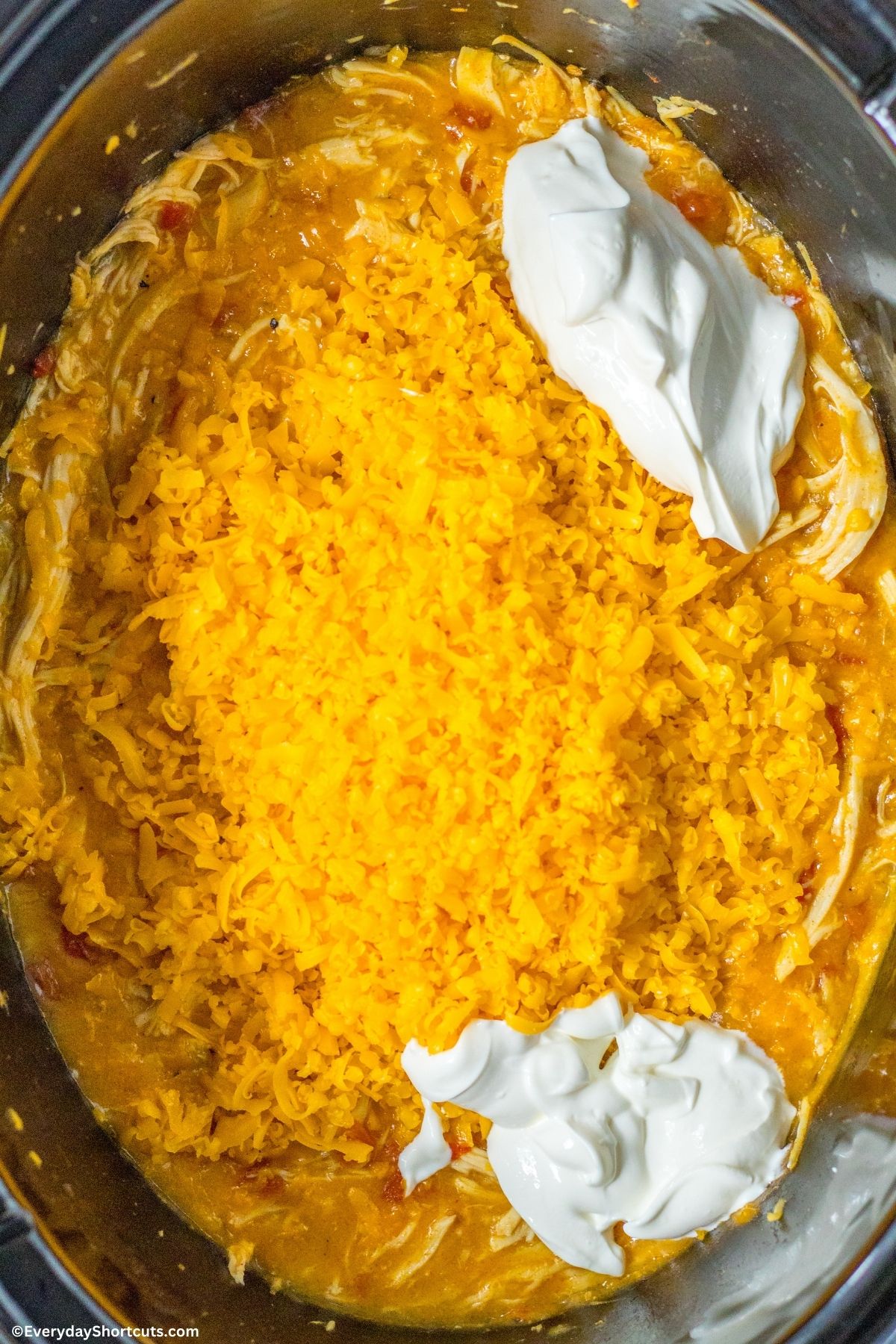 shredded cheese and sour cream on top of chicken in a crockpot