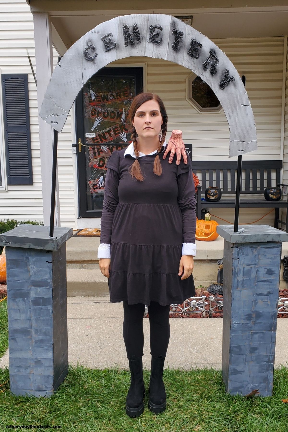 In a Wednesday Addams costume standing under homemade cemetery entrance