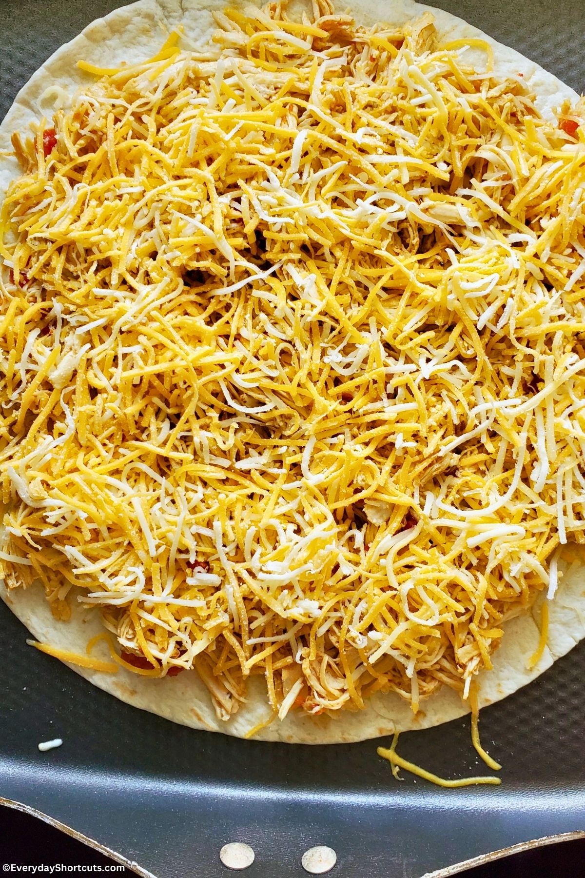 shredded cheese on top of shredded chicken mixture on a tortilla