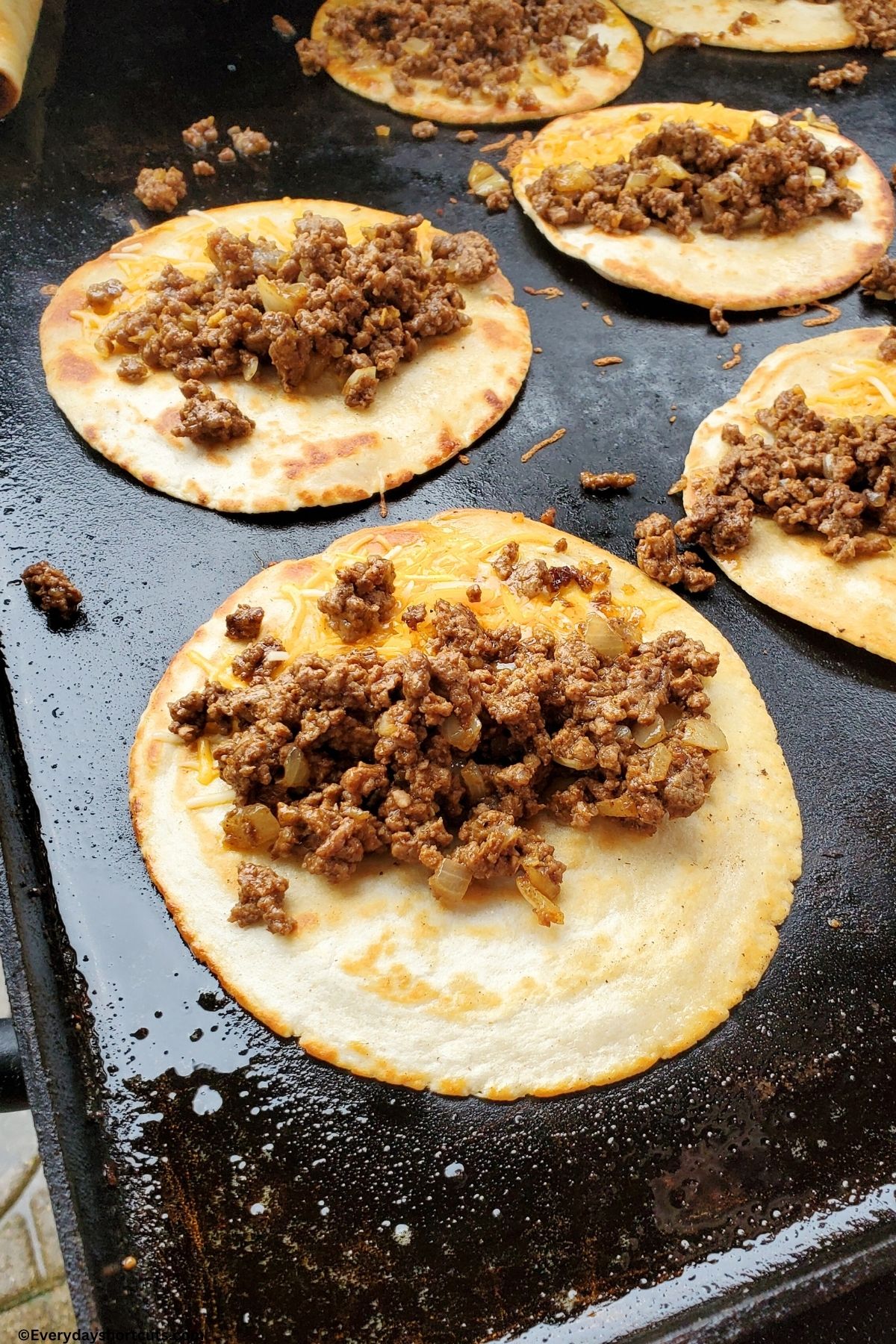 ground beef and cheese on a crispy tortilla on griddle