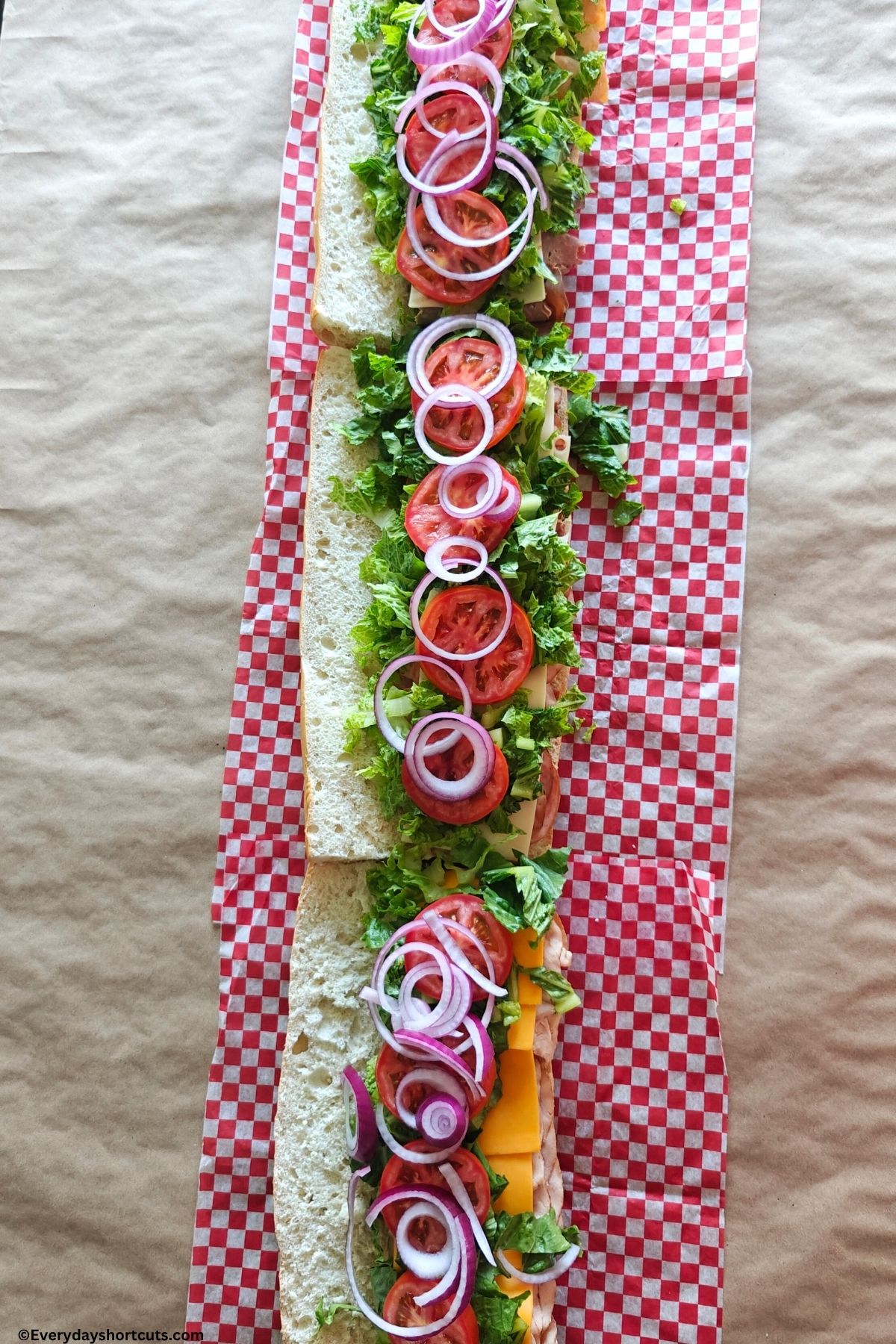 lettuce onion and tomato on top of cheese and lunch meat on bread