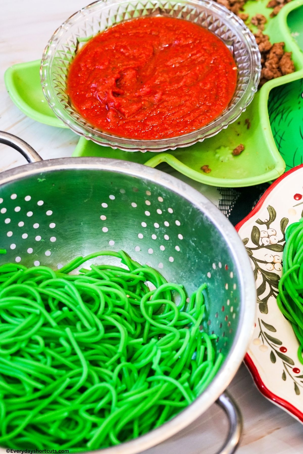 green spaghetti noodles in a colander and pasta sauce in a bowl