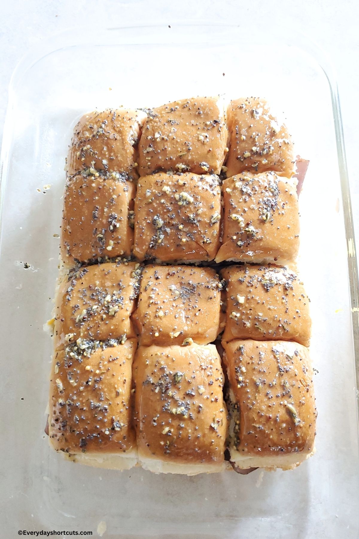 melted butter dried onions and poppy seed mixture brushed over top of Hawaiian roll sliders in a baking dish