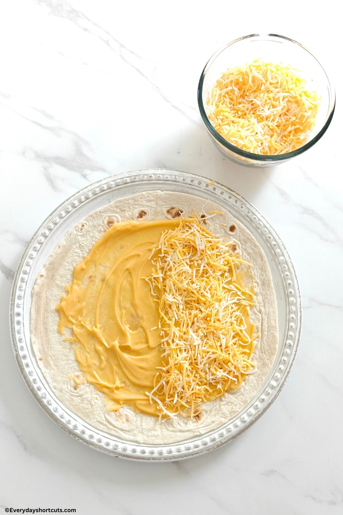 flour tortilla with nacho cheese sauce and shredded cheese on top on a white plate