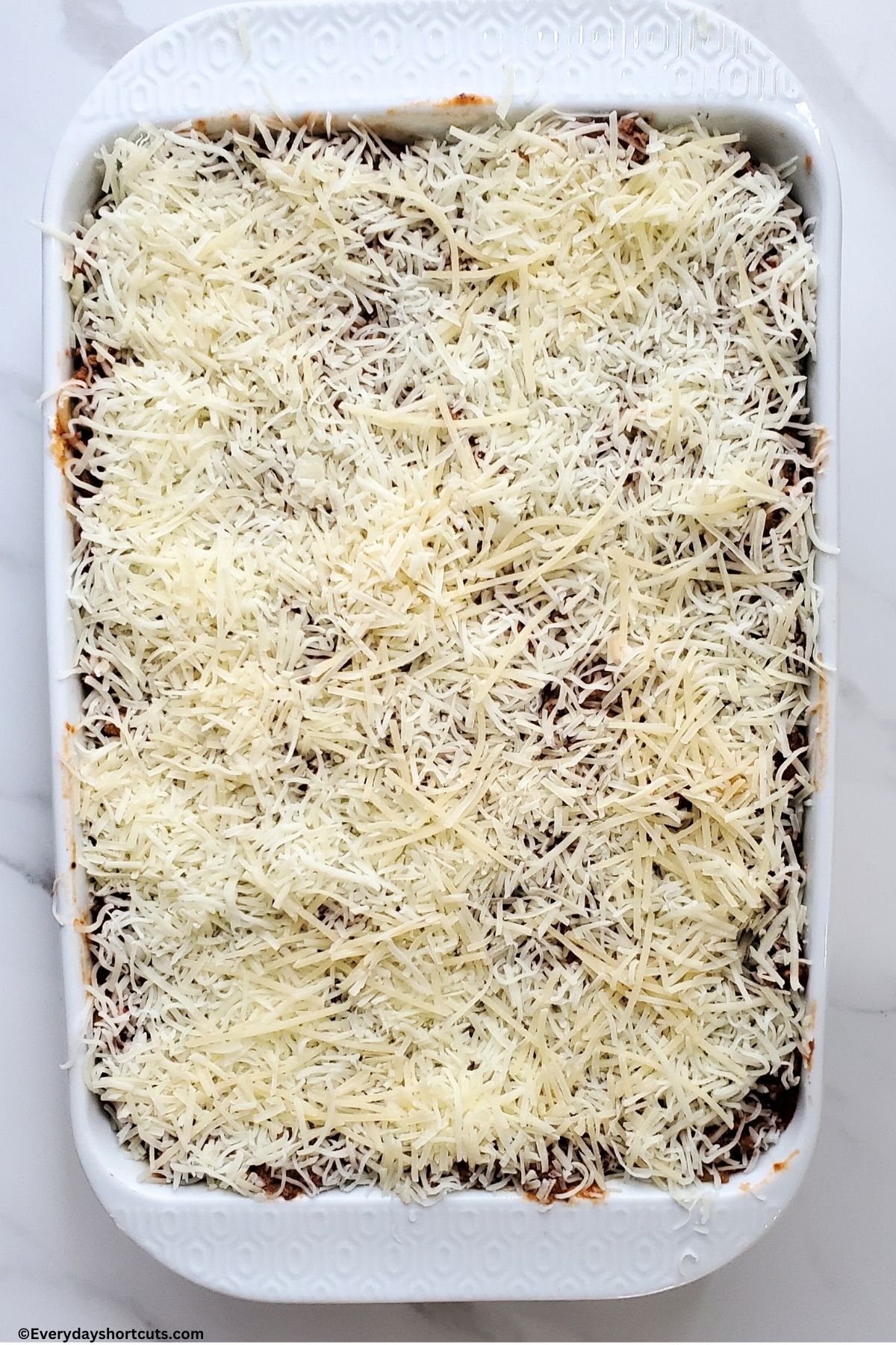 mozzarella and parmesan shredded cheese on top of million dollar spaghetti in a white casserole dish