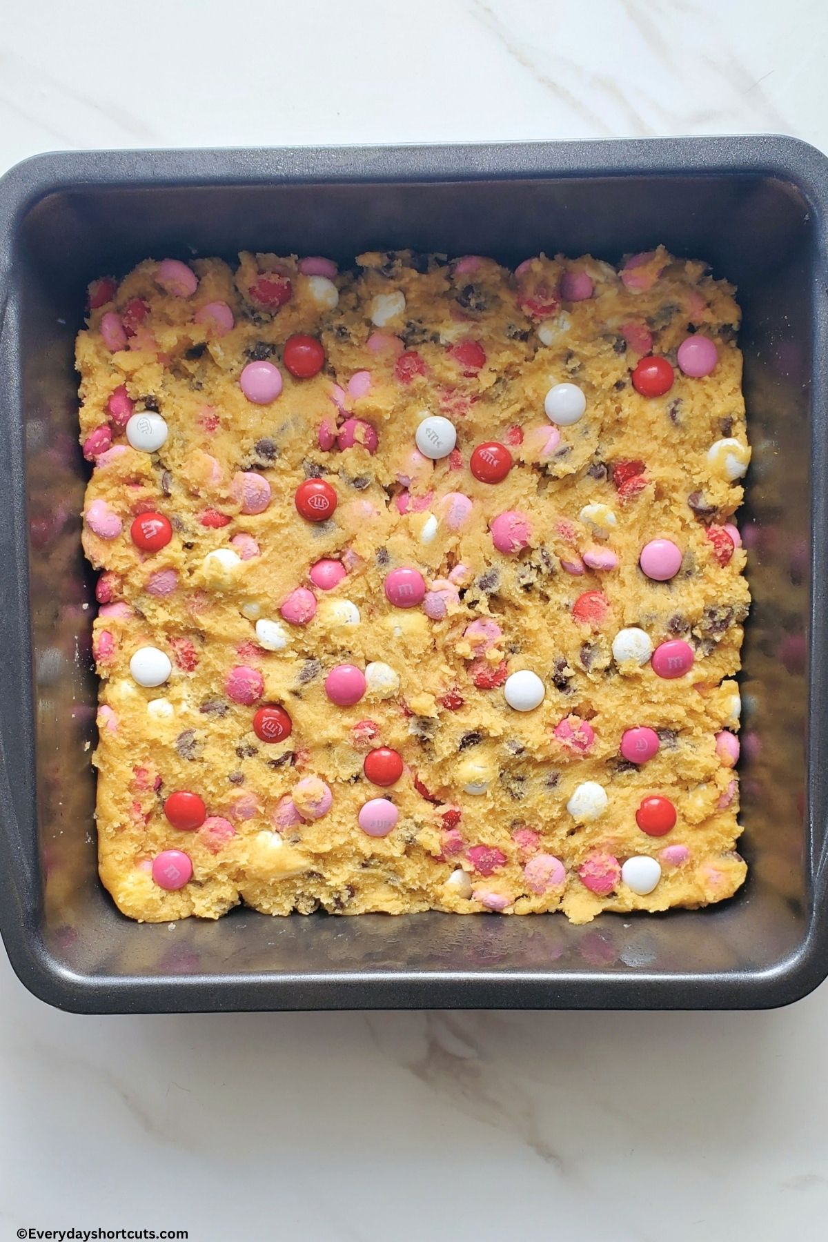 chocolate chip cookie dough with M&Ms pressed down in a baking pan