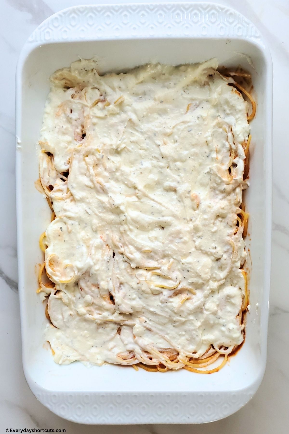 creamy cheese mixture on top of spaghetti noodles in a white baking dish