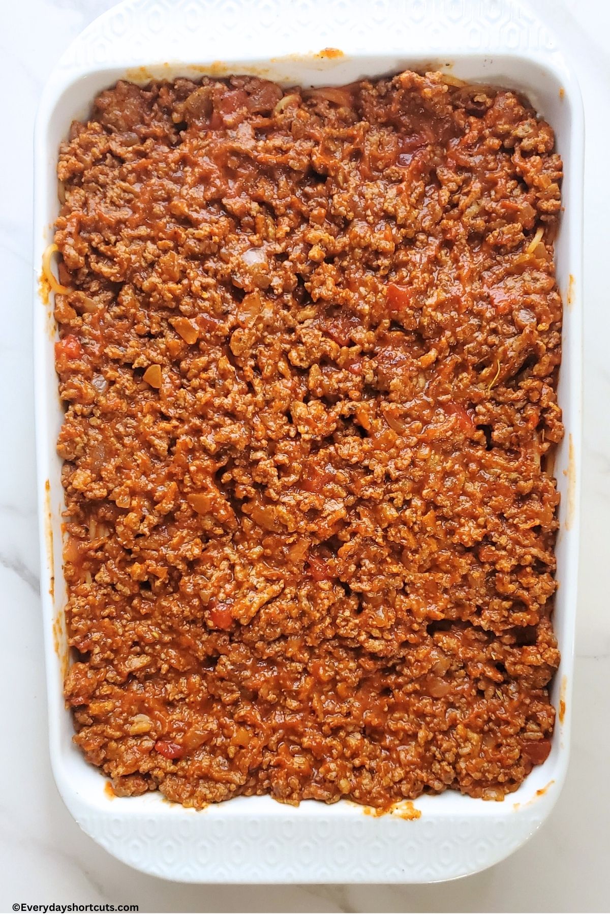 meat sauce on top of spaghetti noodles in a white baking dish