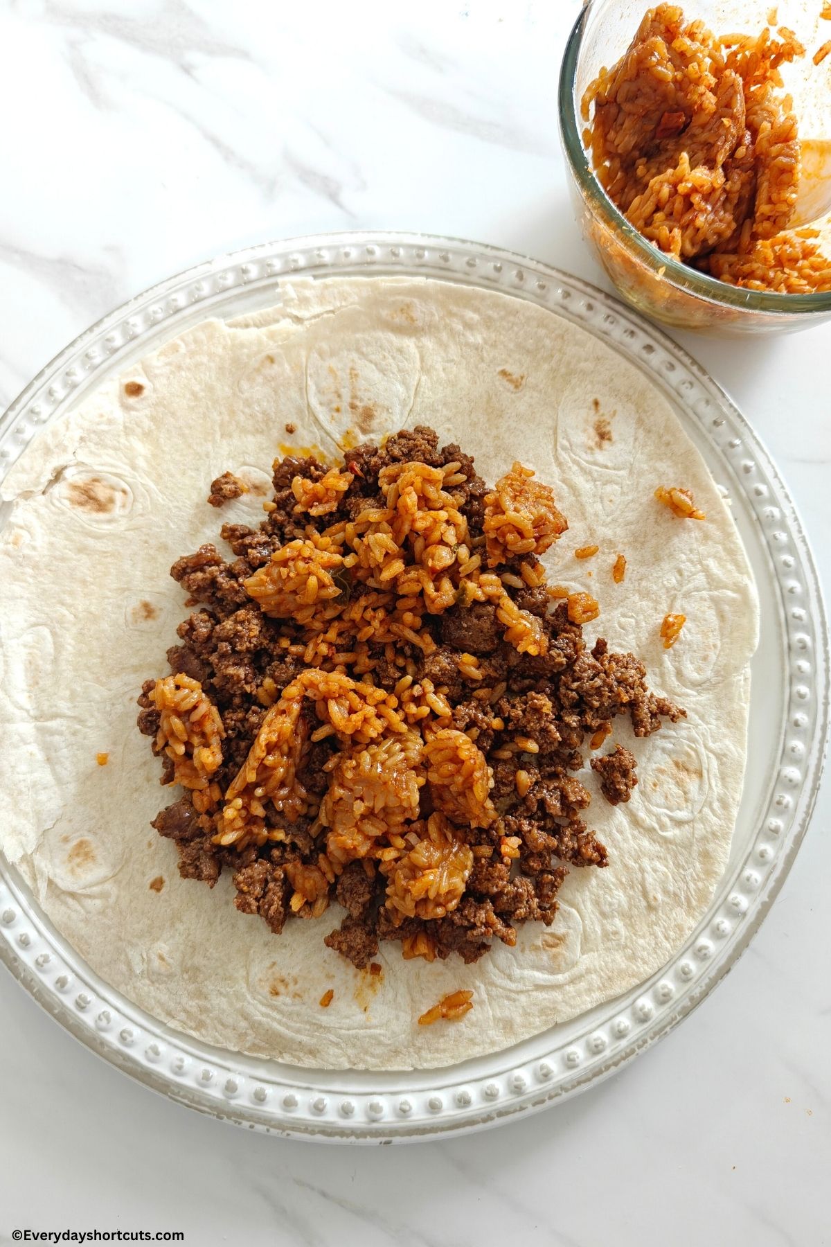 taco meat and Spanish rice on top of a tortilla on a white plate