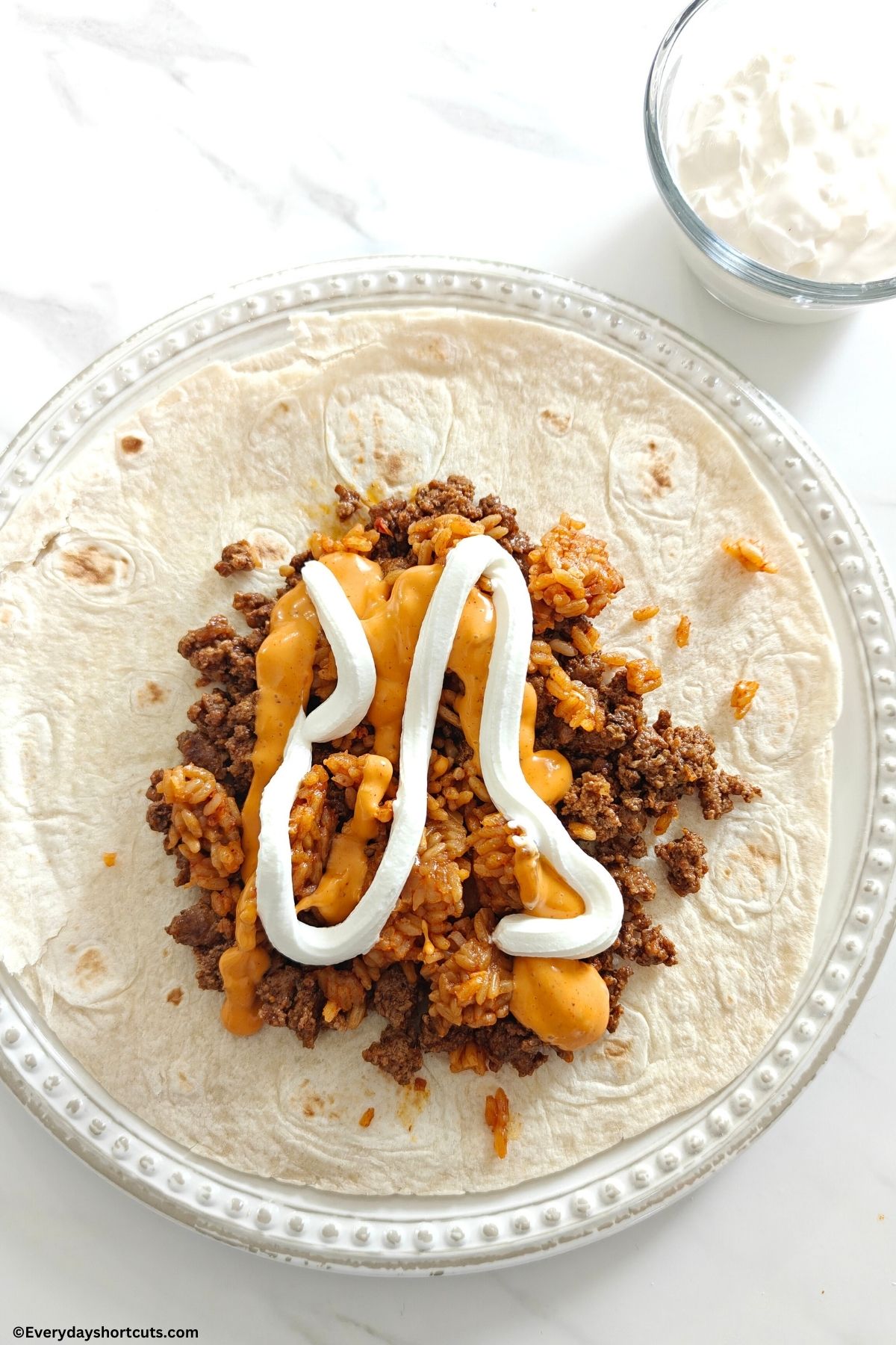 Chipotle sauce and sour cream on top of taco meat and Spanish rice on a tortilla on a white plate