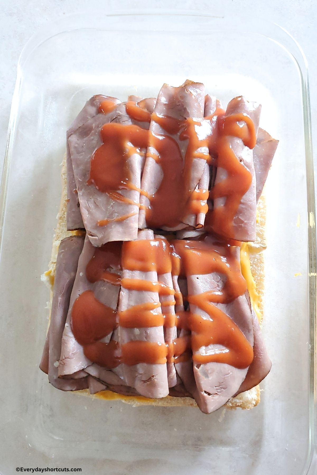 Arby's sauces drizzled over top of roast beef slices with cheese sauce on Hawaiian rolls in a baking dish