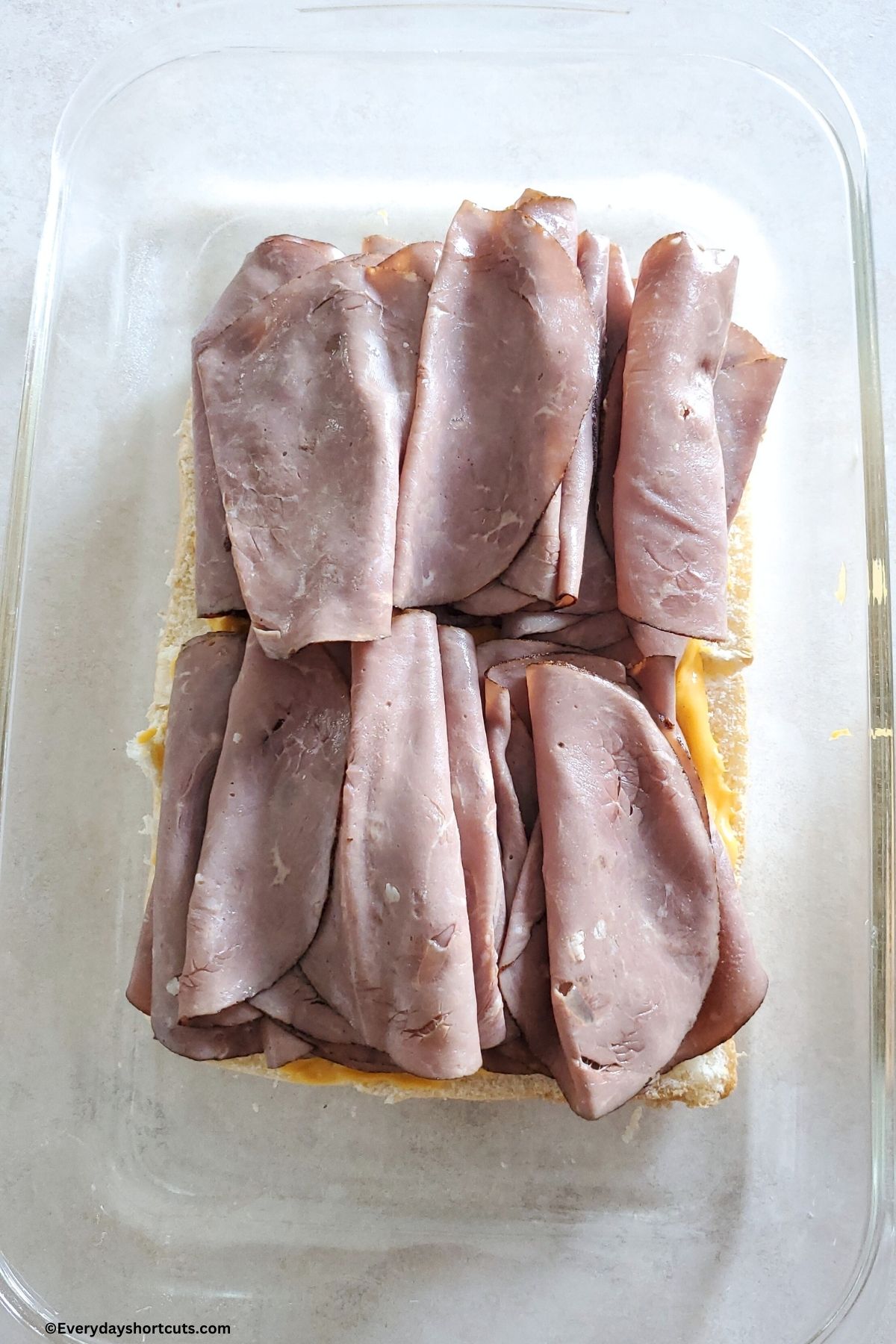 roast beef slices on top of cheese sauce and slider buns in a baking dish