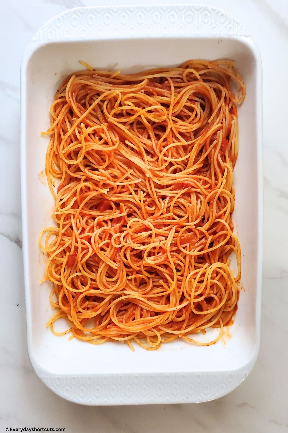 cooked spaghetti noodles with marinara sauce in a white baking dish