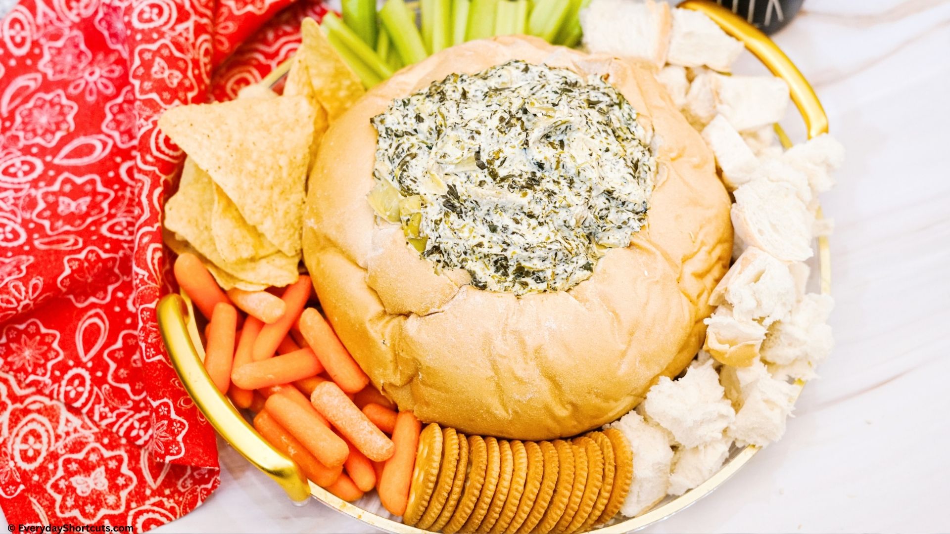 artichoke spinach dip in a bread bowl surrounded by veggies tortilla chips bread and crackers next to a teal color instant pot