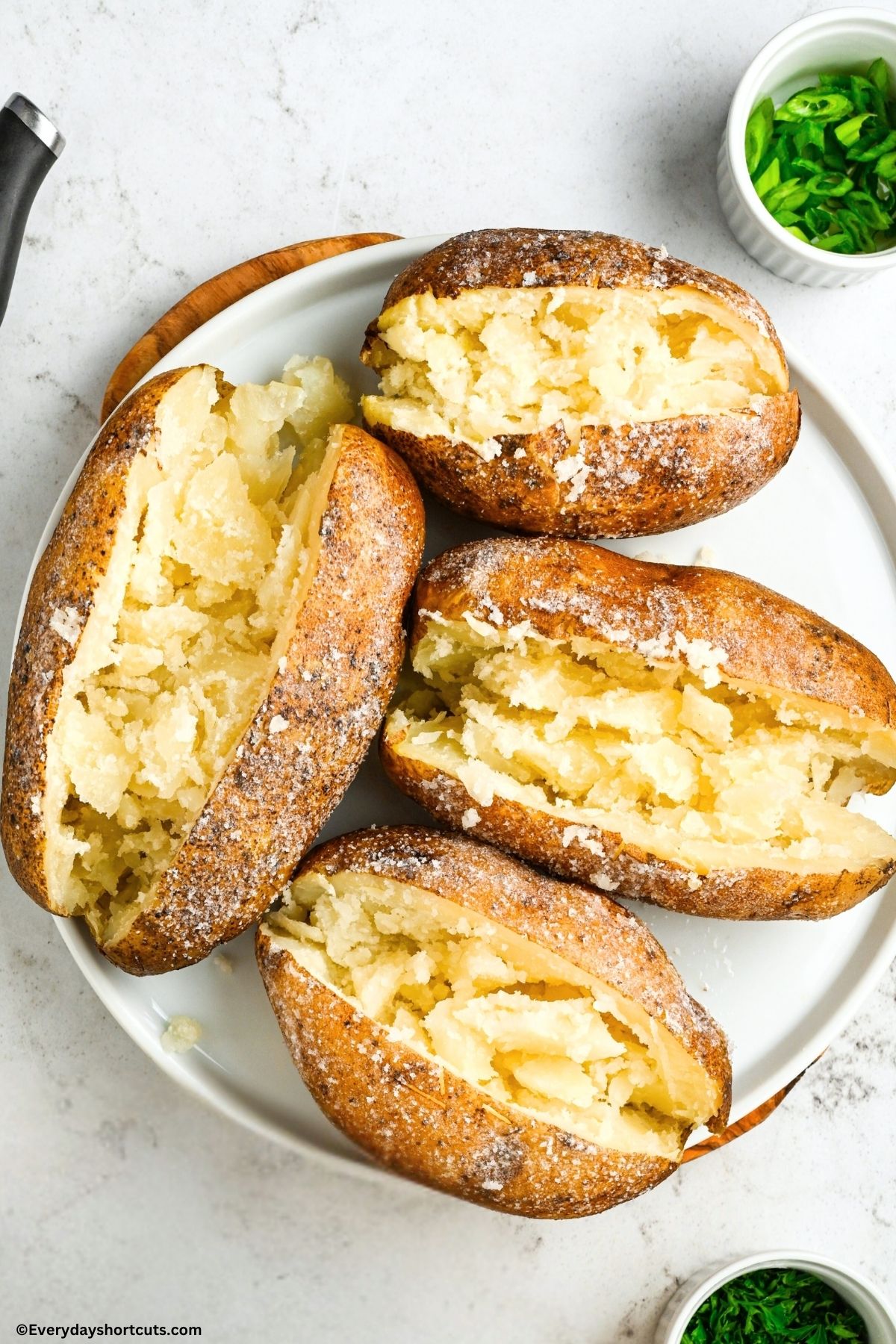baked potatoes on a white plate next to a bowl of green onions