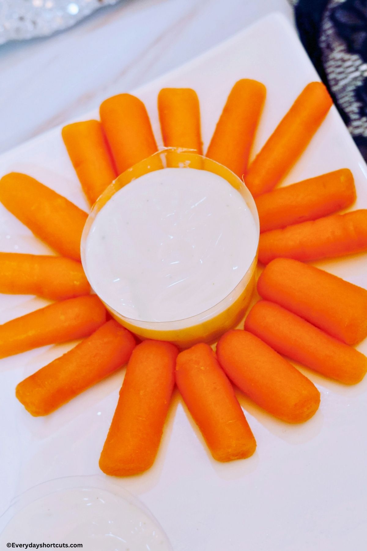 baby carrots in a circular pattern with a bowl of ranch dressing in the middle of it