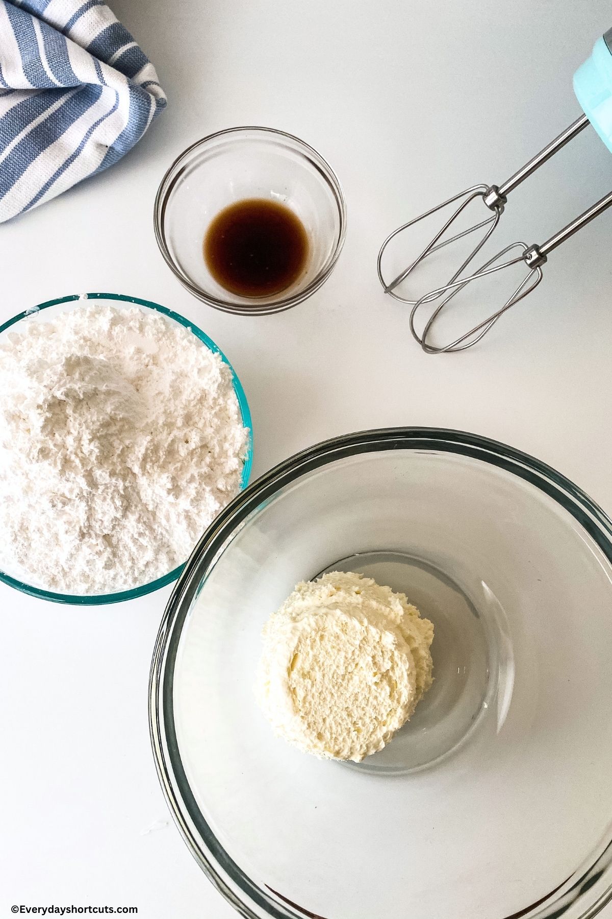 whipped cream in a bowl powdered sugar in a bowl and vanilla extract in a bowl next to electric mixer