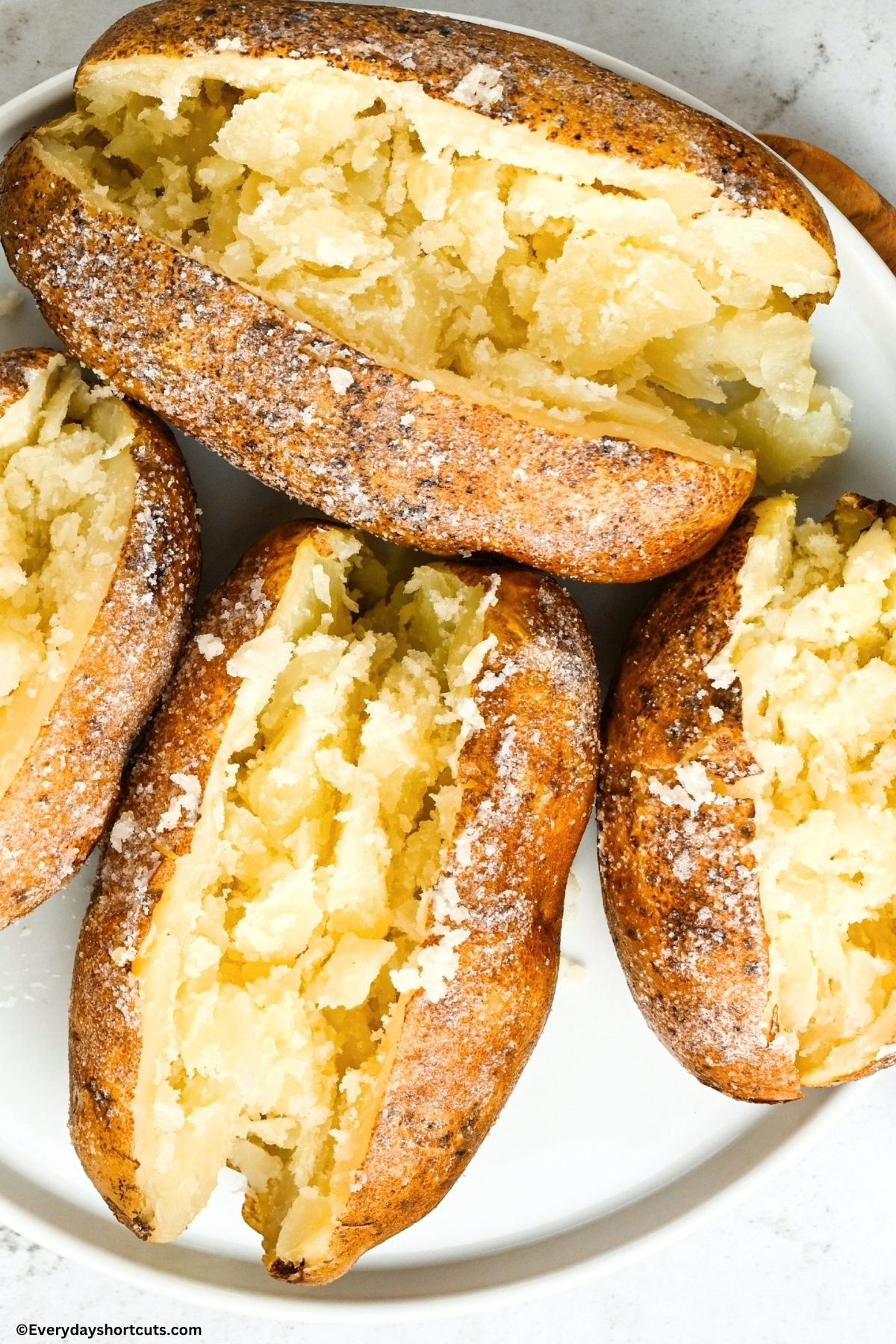 four baked potatoes sliced open on a white plate