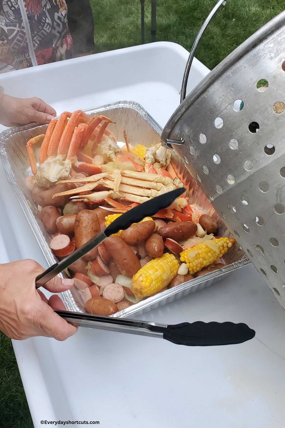 seafood boil mixture in an aluminum pa with tongs