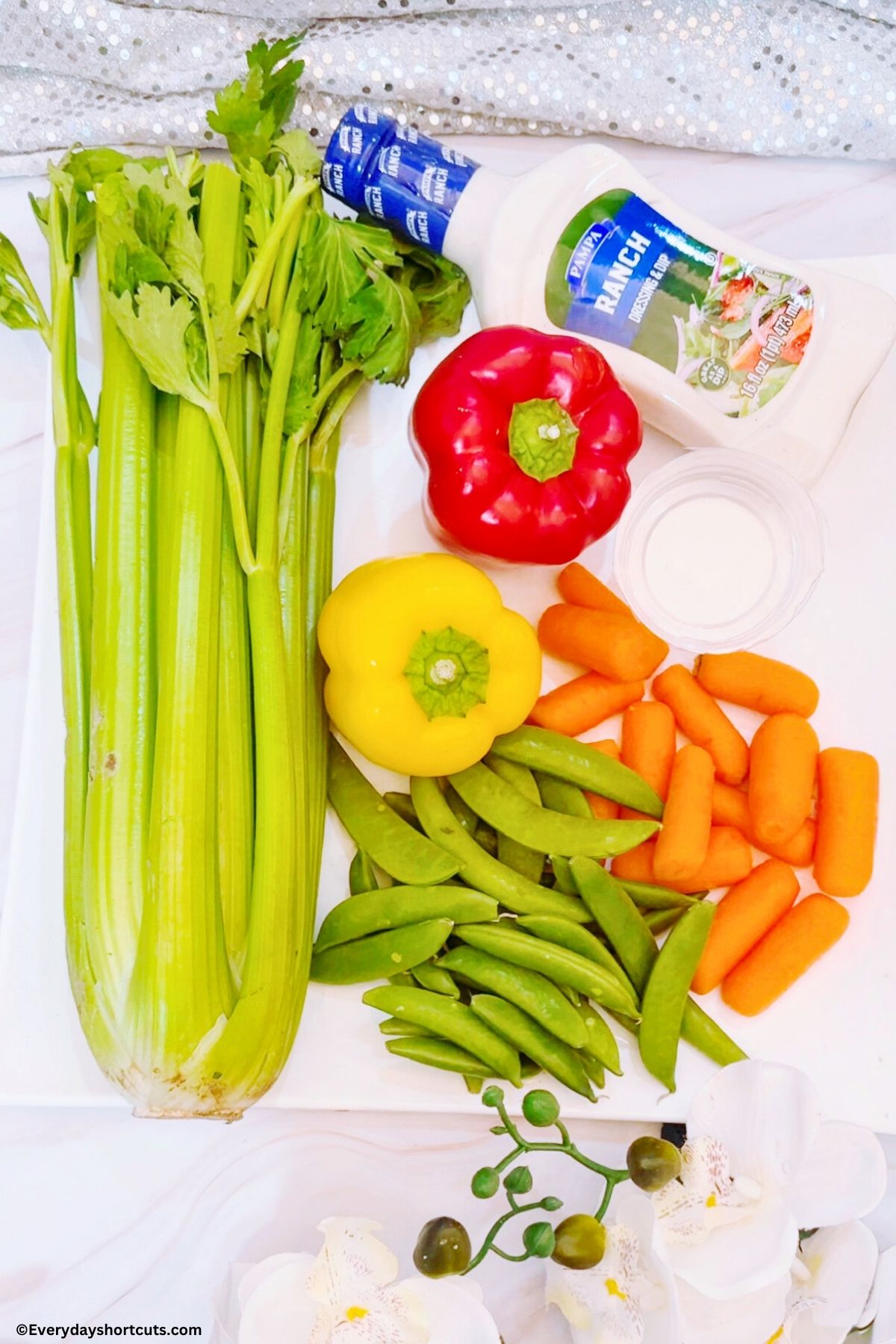 celery stalk red bell pepper yellow bell pepper bowls ranch dressing baby carrot and snap peas on a white board