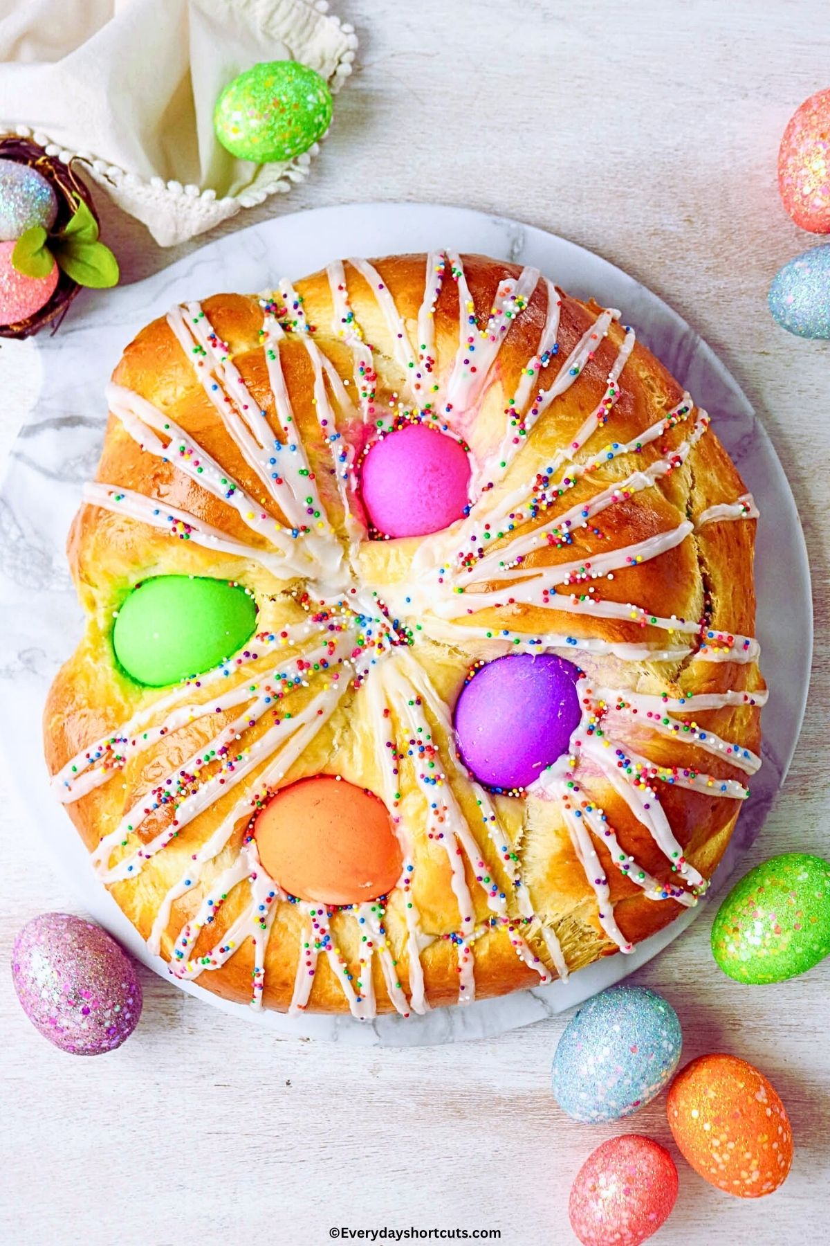 closeup shot above of Easter bread with 4 colored eggs, icing and sprinkles on top