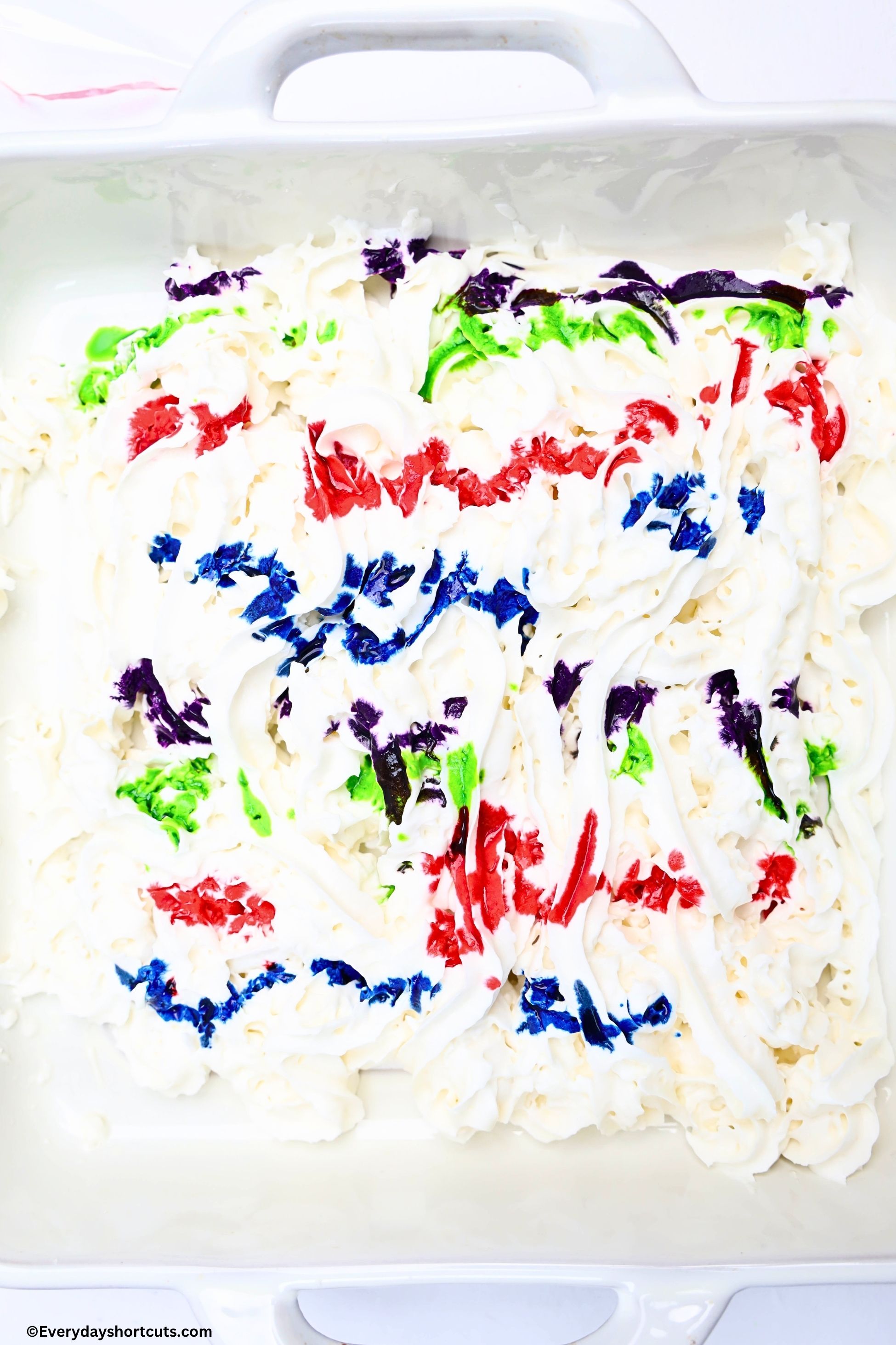 whipped cream in a white baking dish with drop of food coloring on top of whipped cream
