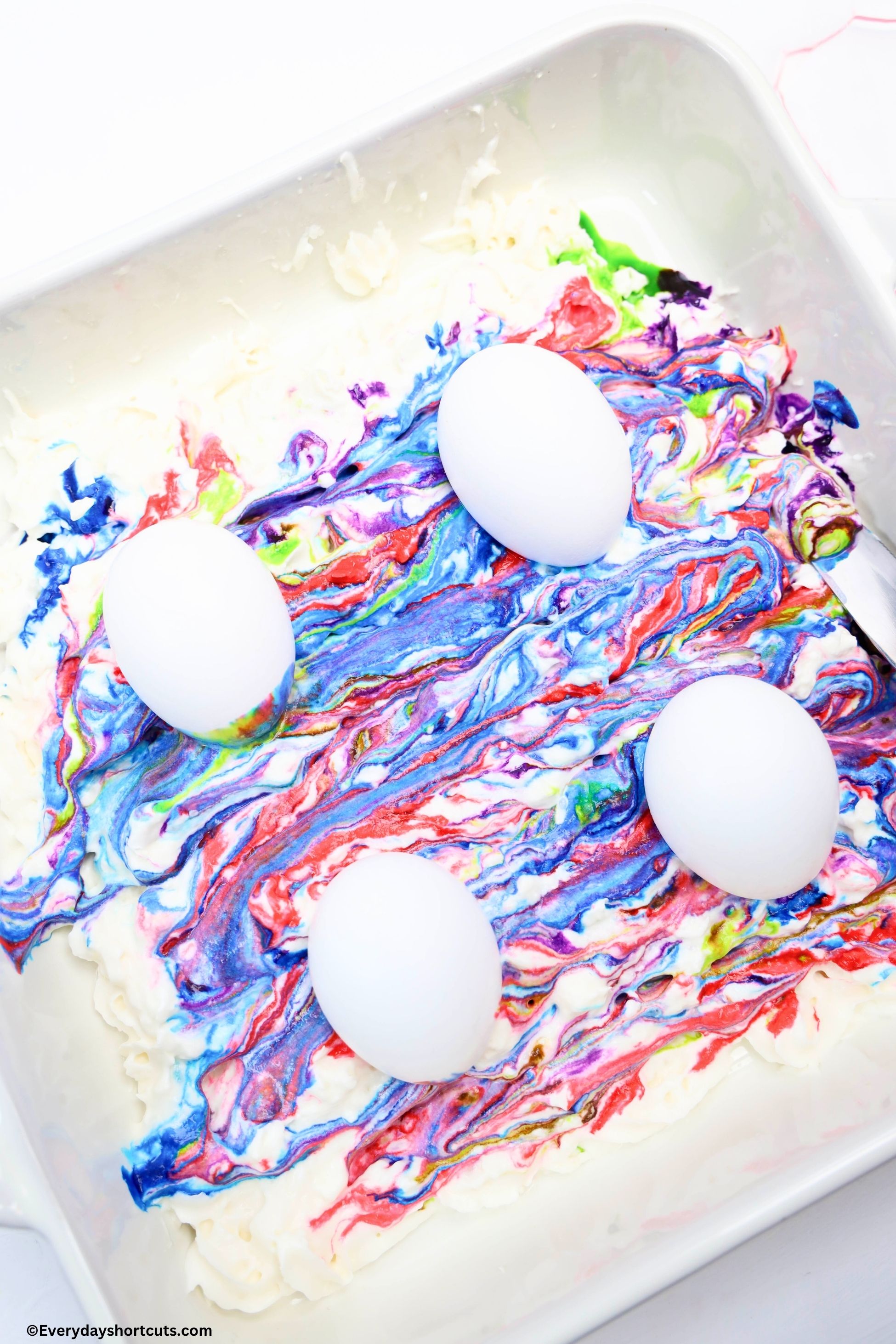 eggs sitting on top of swirled food coloring and whipped cream in a white baking dish