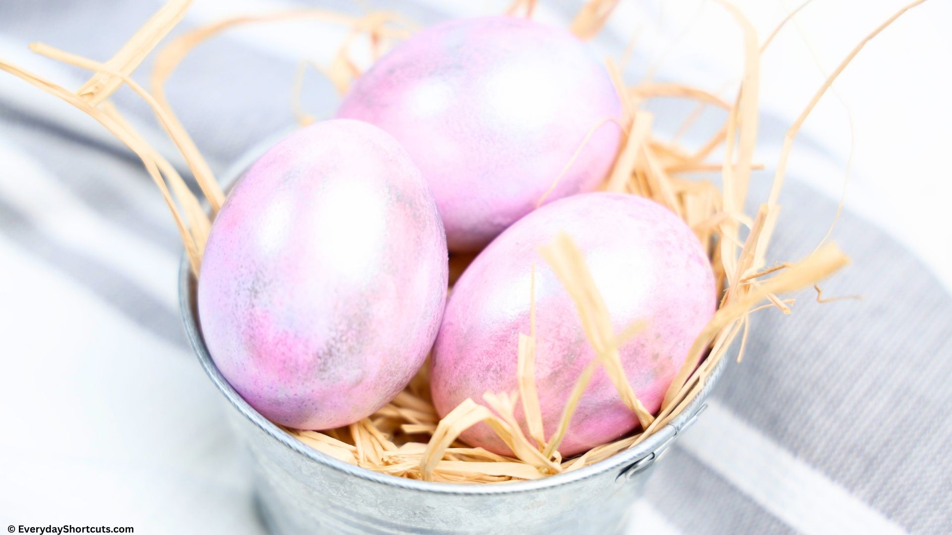 side shot of whipped cream dyed Easter eggs in a silver bucket with hay