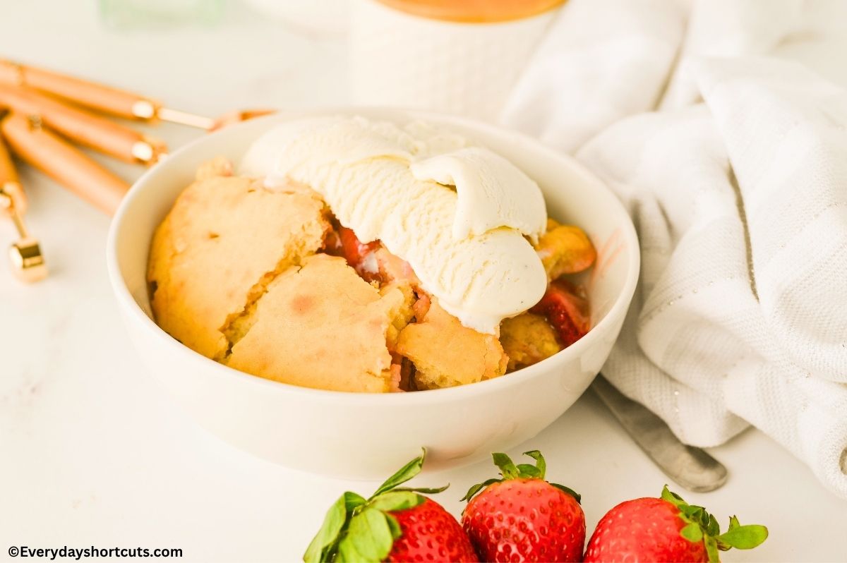 a bowl of strawberry cobbler with vanilla ice cream on top next to 3 strawberries