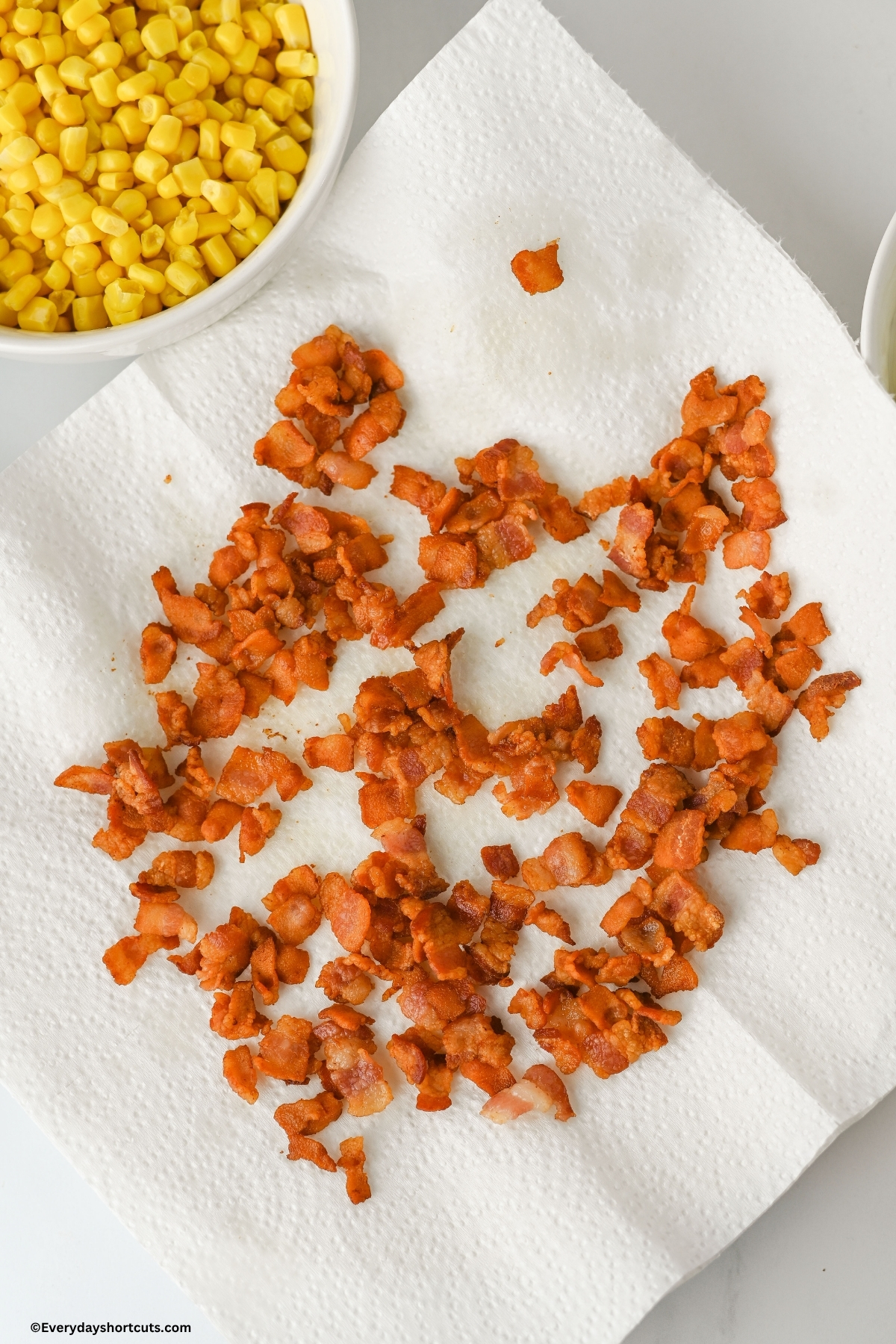 cooked bacon cut into pieces on a paper plate lined with a paper towel next to a bowl of corn