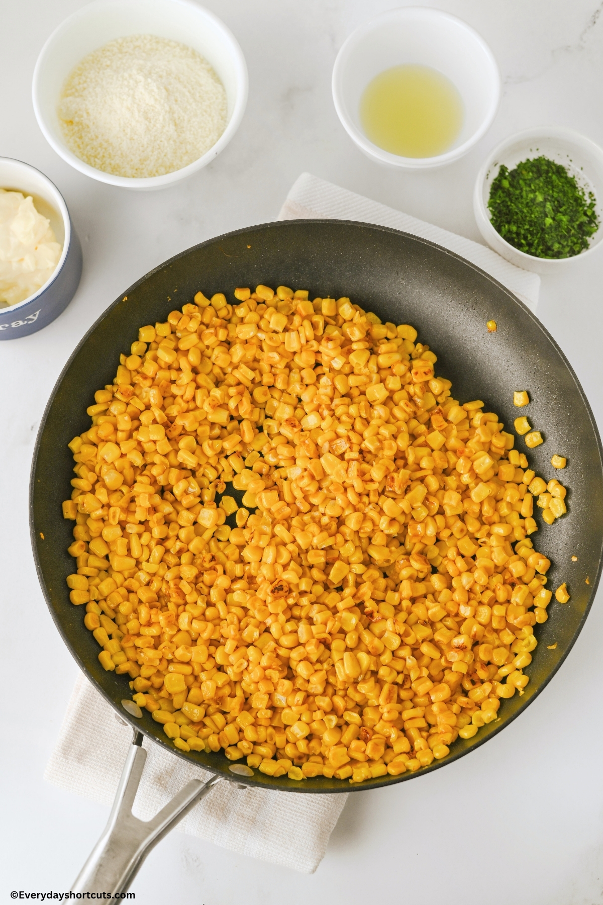 charred corn in a pan next to bowls of mayo, cotija, lime juice and cilantro