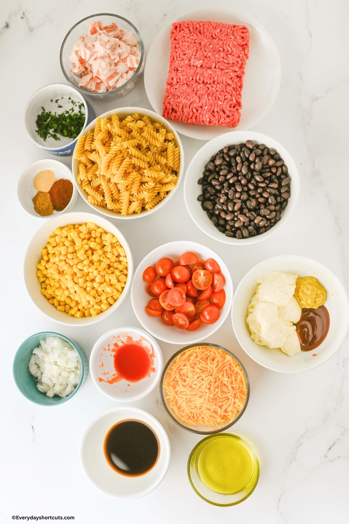 ingredients shown: Pasta, Bacon
Ground Beef, Olive Oil, Whole Kernel Corn, Black Beans, Grape Tomatoes, Onion, Shredded cheddar cheese, Mayonnaise, barbeque sauce, spicy brown mustard, Worcestershire sauce, and hot sauce, Chili powder, cumin, garlic powder, salt, pepper and fresh cilantro