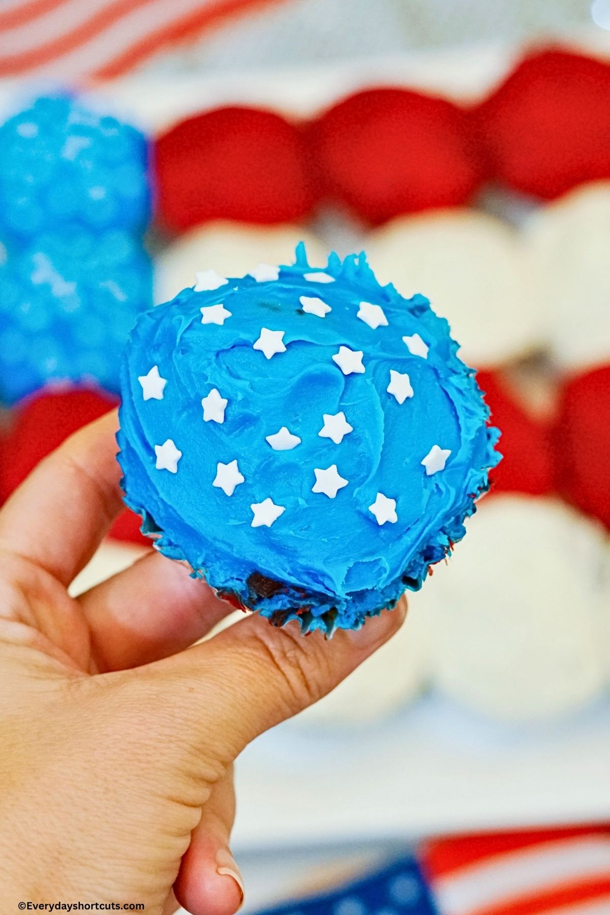 holding a blue frosted cupcake with white stars sprinkles