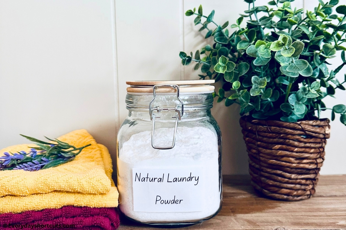 Homemade Powder Laundry Detergent in a glass jar next to yellow and red folded towels and a fake plant