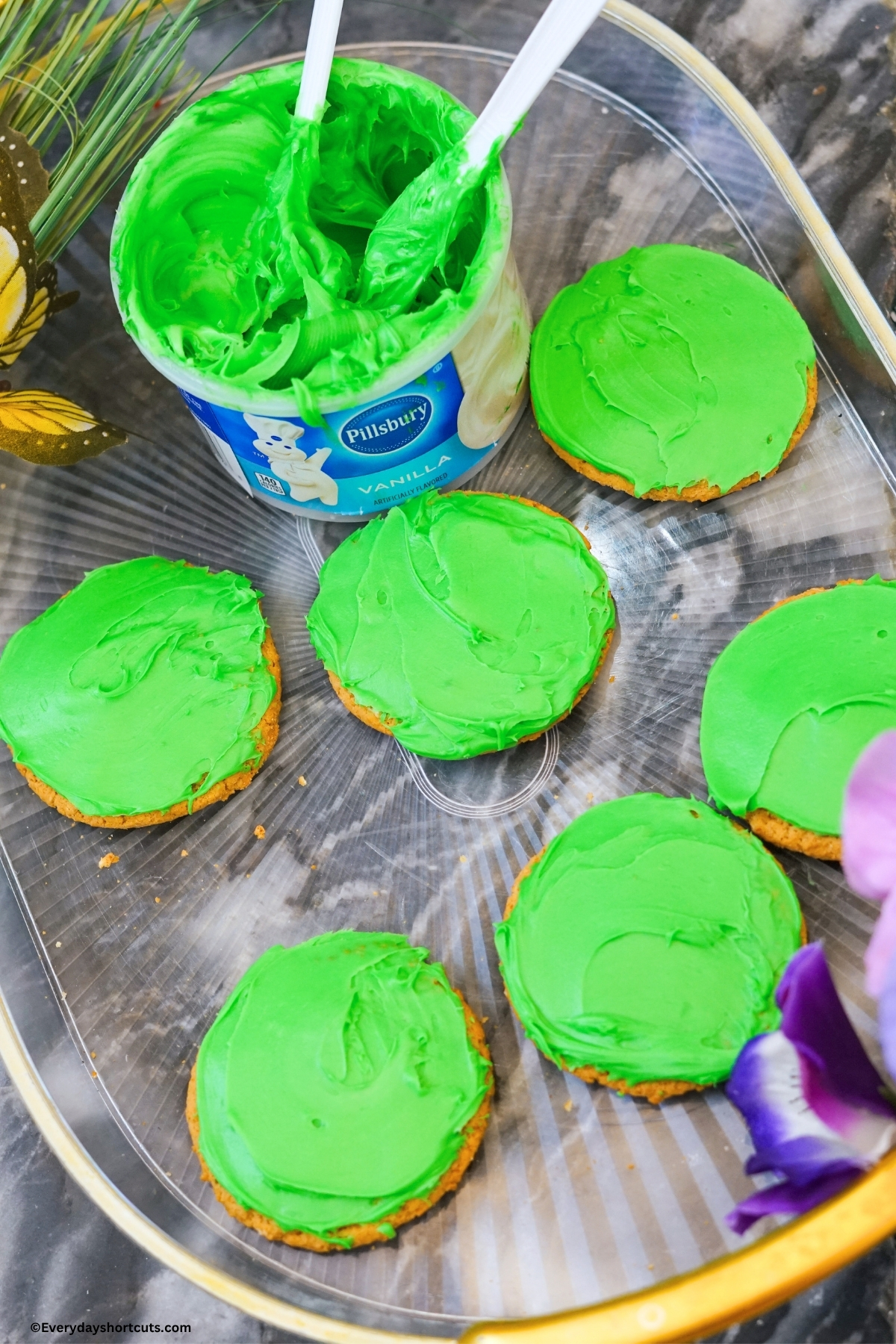 green frosting on sugar cookies next to a tub of green colored frosting