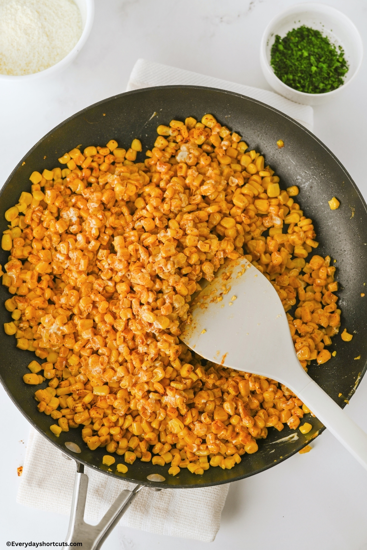 charred corn in a pan with a spoon and creamy sauce mixed in