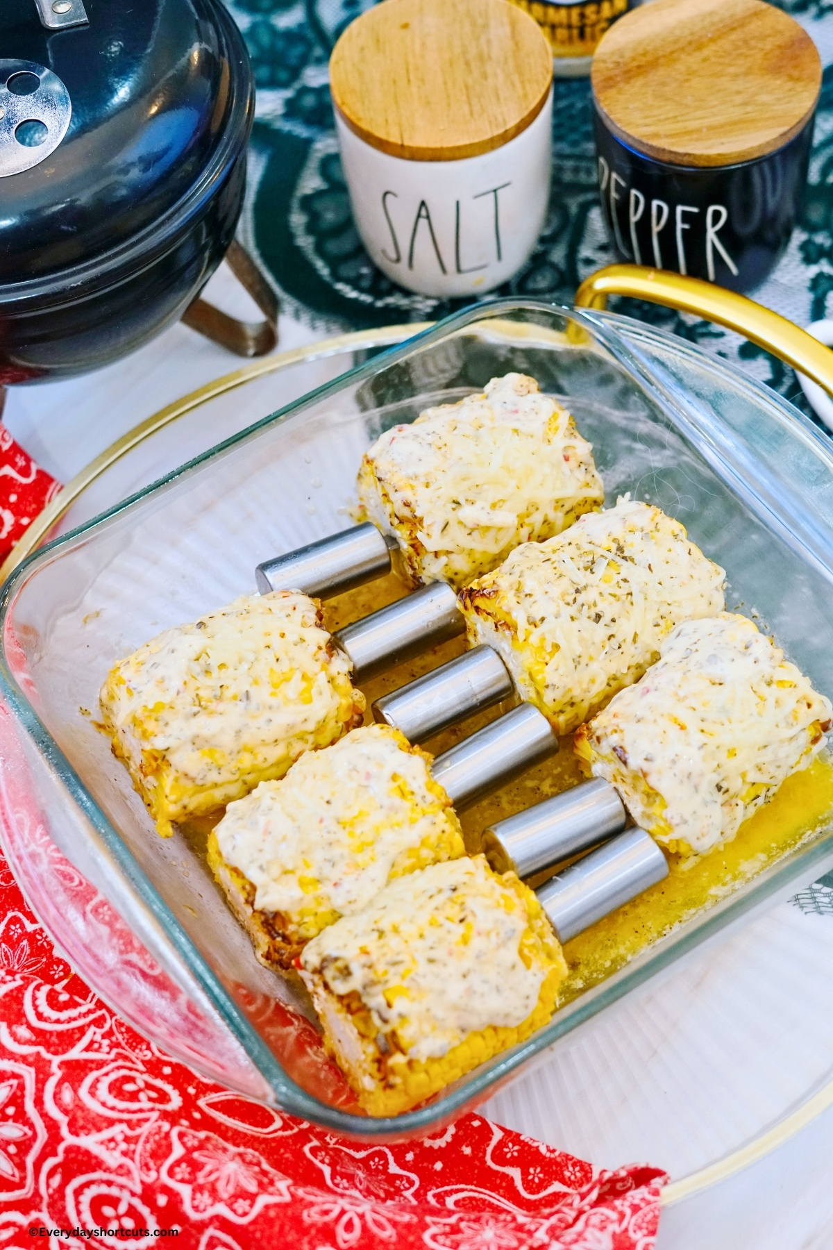 buttered corn on the cob with shredded parmesan cheese and parmesan garlic sauce in a baking dish next to a red napkin