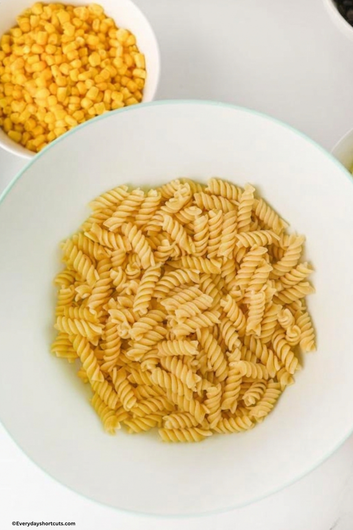 cooked pasta al dente in a white bowl next to a bowl of corn