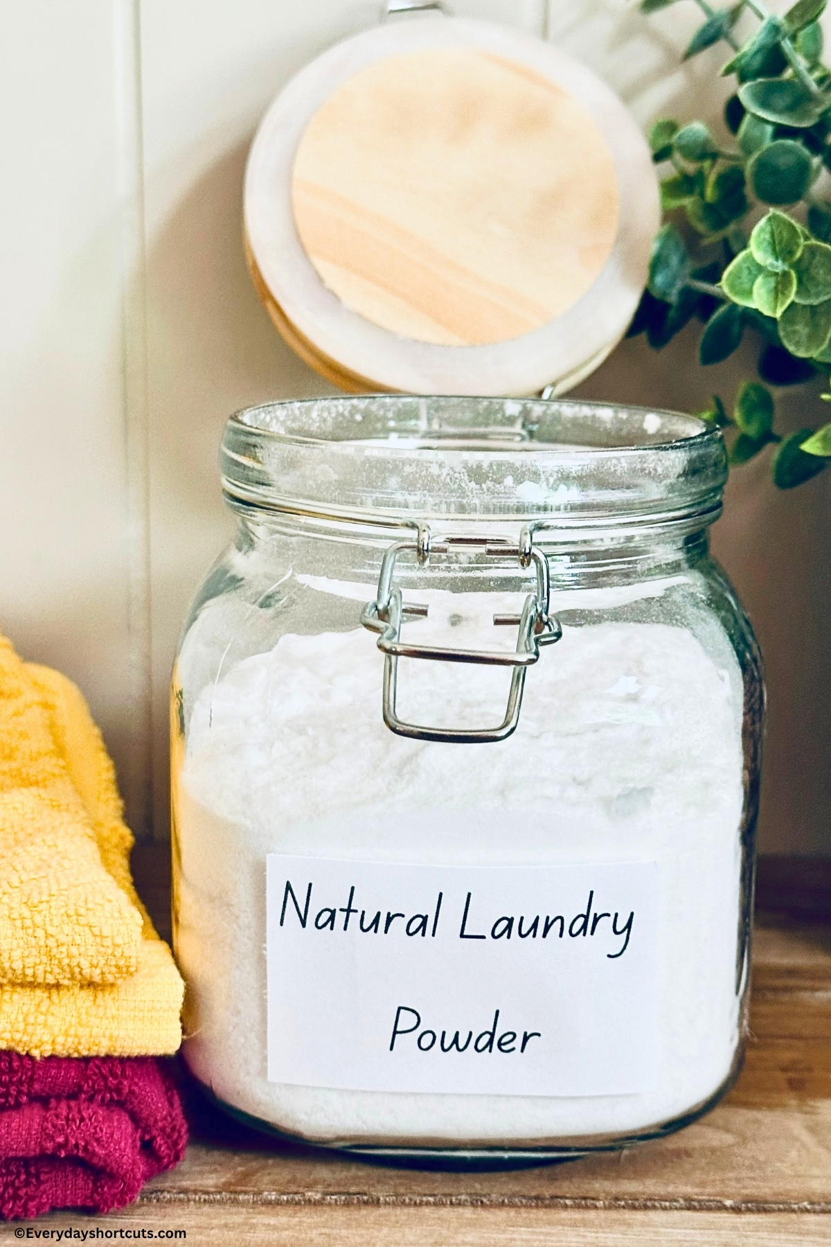homemade powder laundry detergent in a glass jar next to folded towels