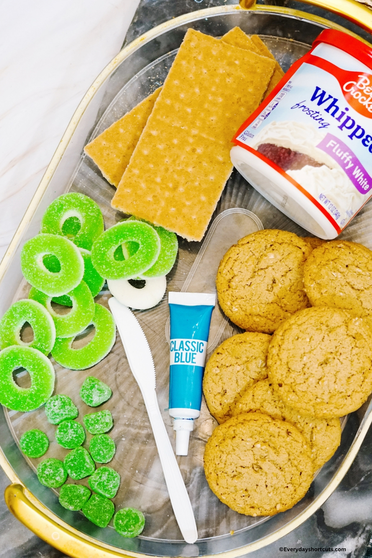 ingredients shown: graham crackers, white frosting, green gummy rings, blue food coloring, sugar cookies, green gum drops