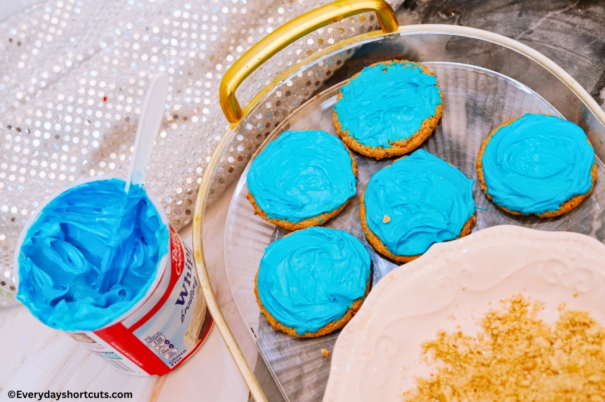 sugar cookies frosting with blue frosting on a platter next to crushed graham crackers