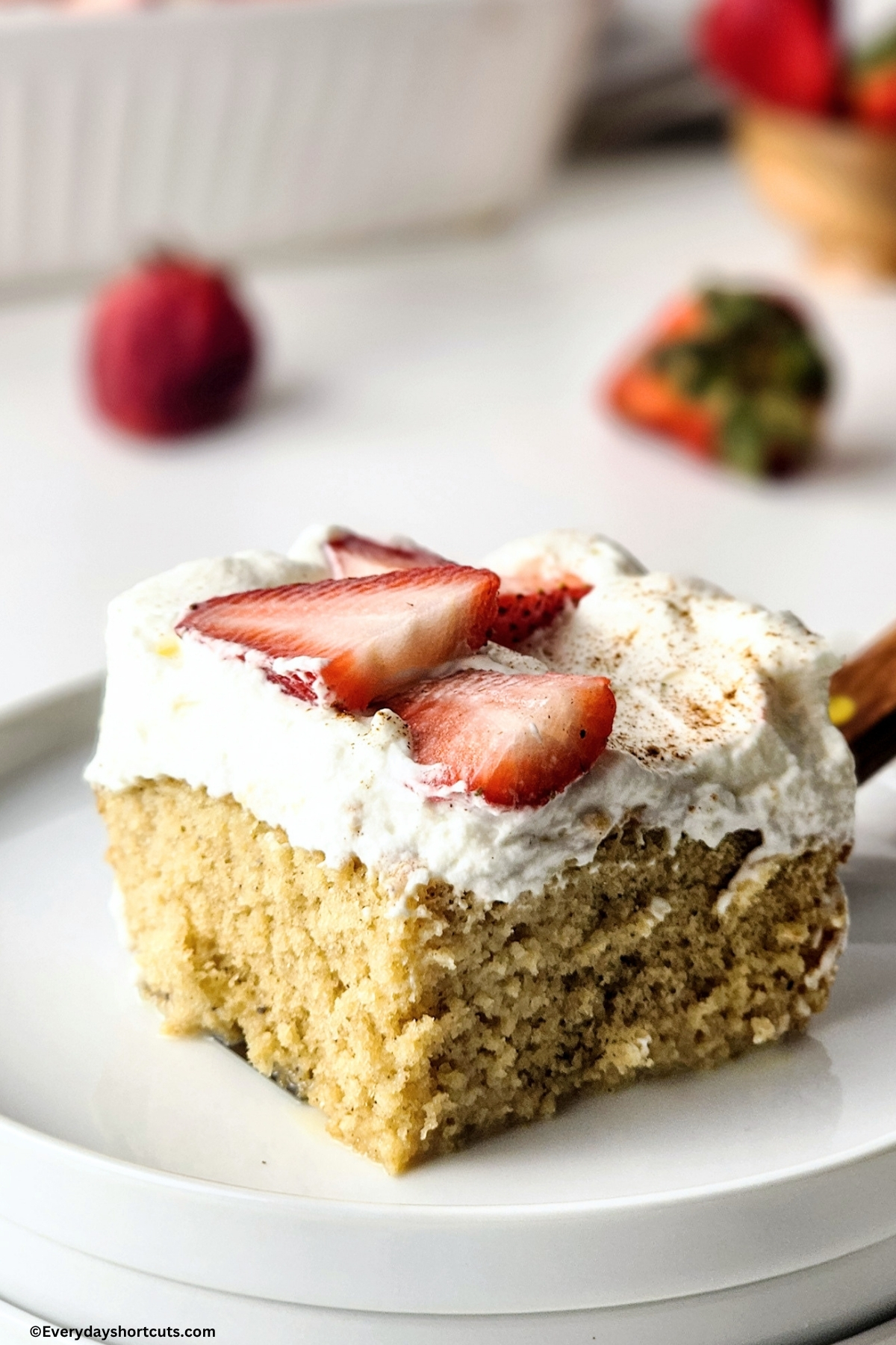 slice of tres leches cake on a white plate garnished with strawberries and cinnamon