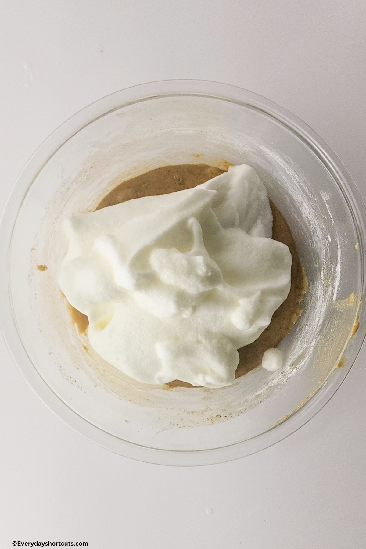 stiff peak egg whites on top of cake batter in a bowl