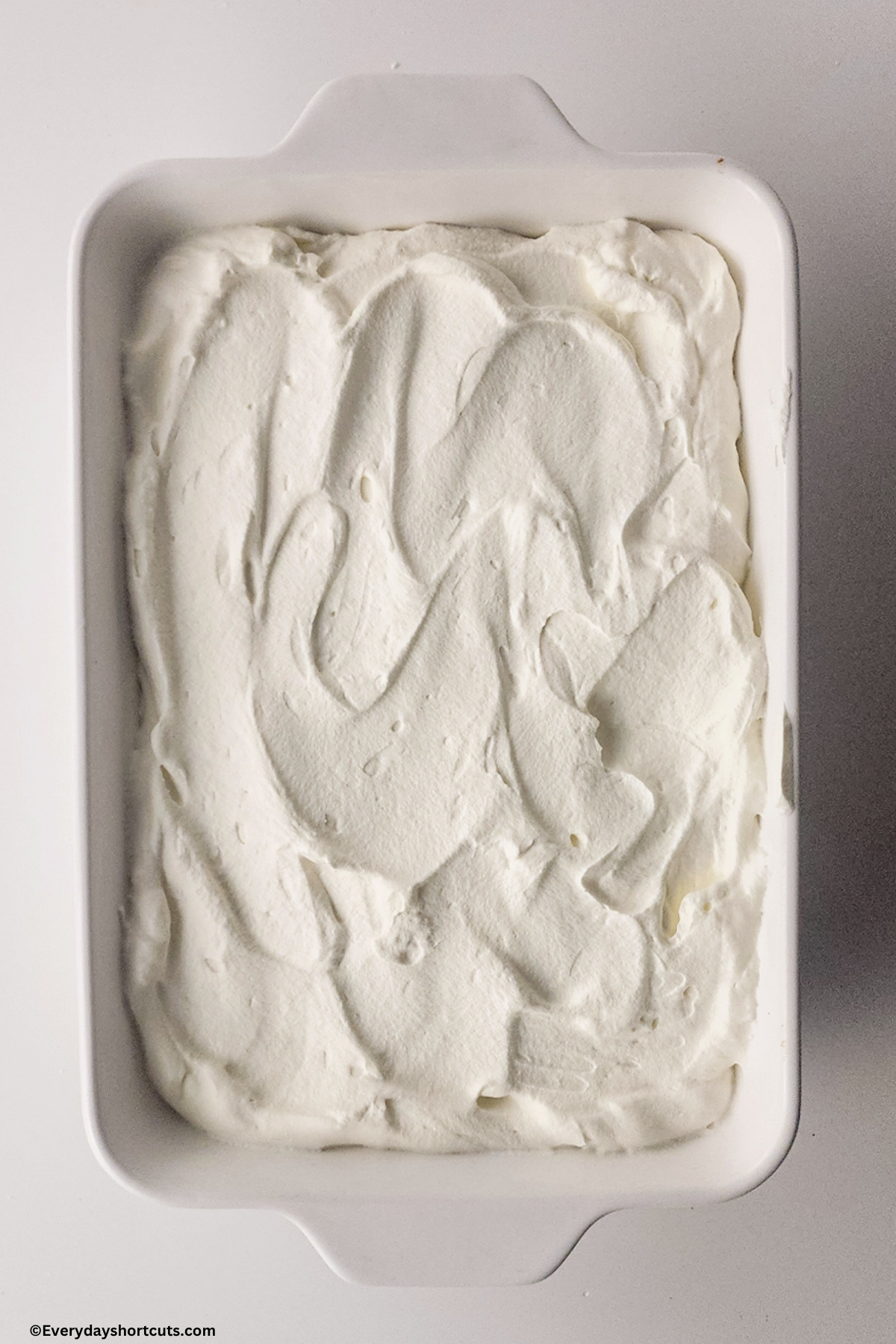 whipped topping spread on top of tres leches cake in a white baking dish